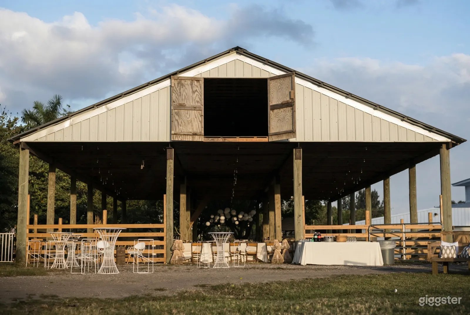 A large open barn like structure with decorative tables outside and long tables with chairs inside.