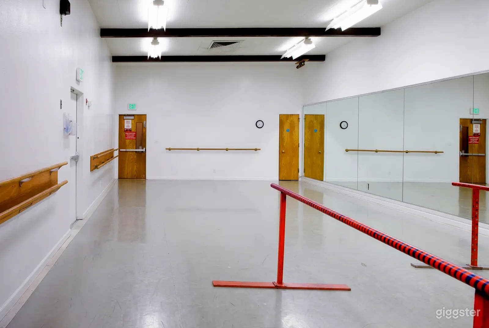 A red exercise bar sits in the center of a dance studio with a mirrored wall.