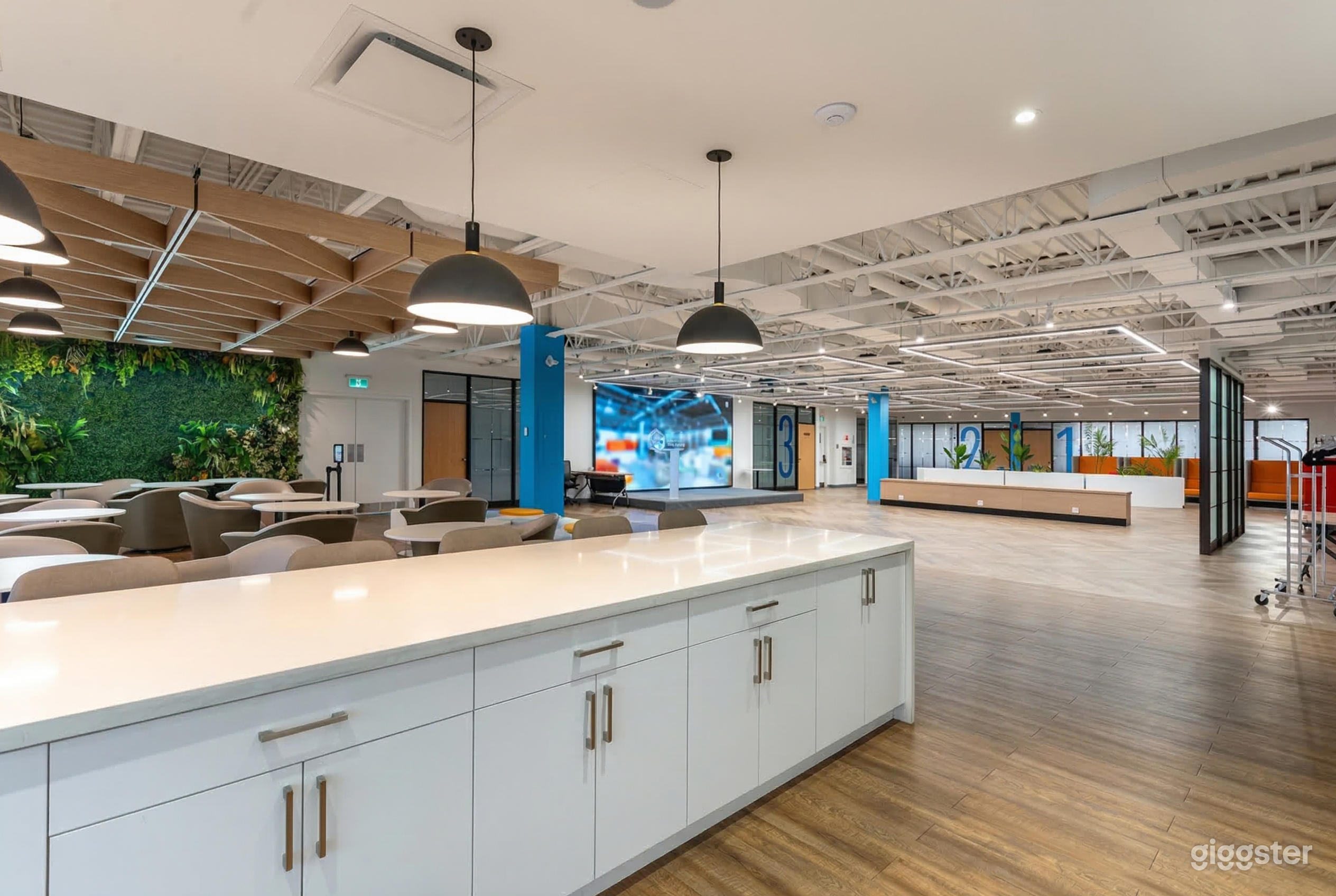 A long white cabinet with tables and chairs sits to the left of an open presentation area with a floor to ceiling screen.