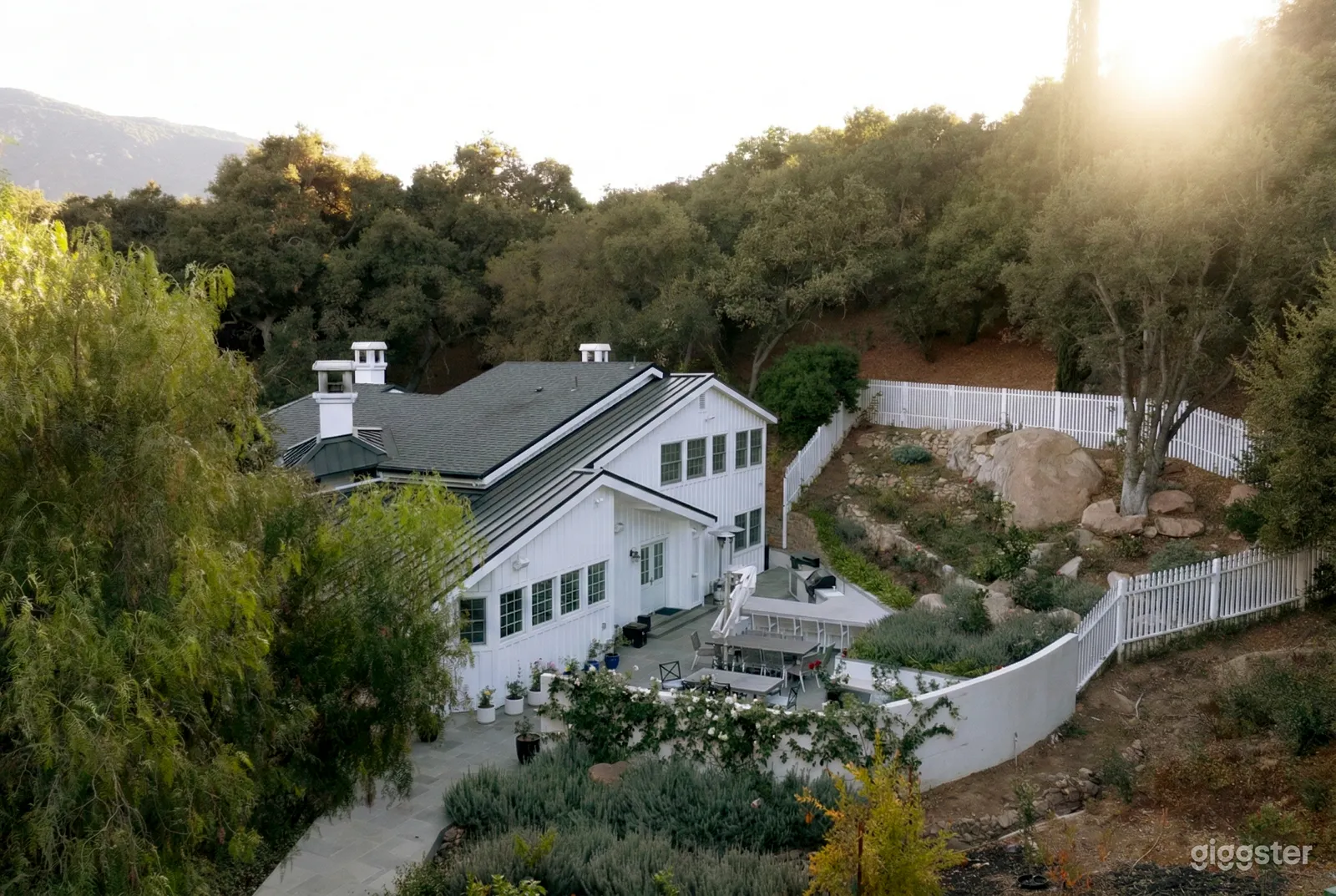 A large white house sits in front of a terrace with covered areas by a big rock garden.