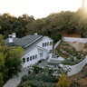 A large white house sits in front of a terrace with covered areas by a big rock garden.