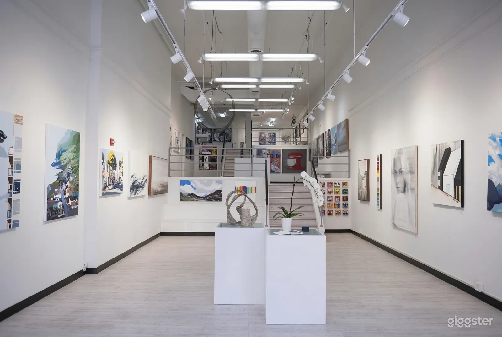 An art gallery room painted in white with varying styles and shapes of paintings in the main and upper level.