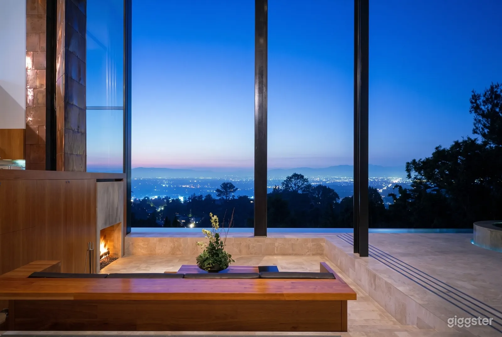 A modern looking empty space with cement floors and a fireplace overlooks a city through floor to ceiling windows.