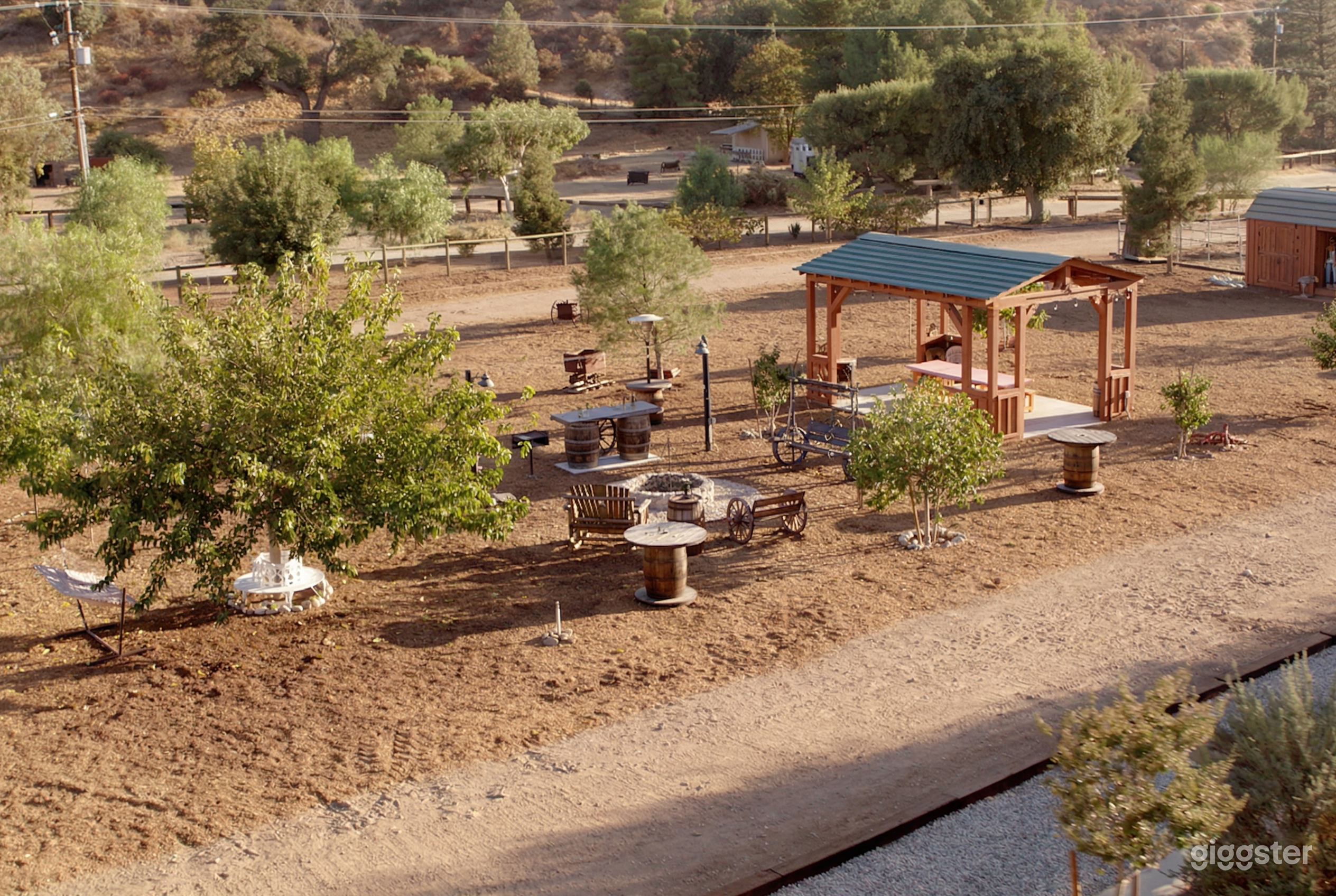 A ranch style property with wagon wheel benches, barrel tables, and an open covered shelter outside.