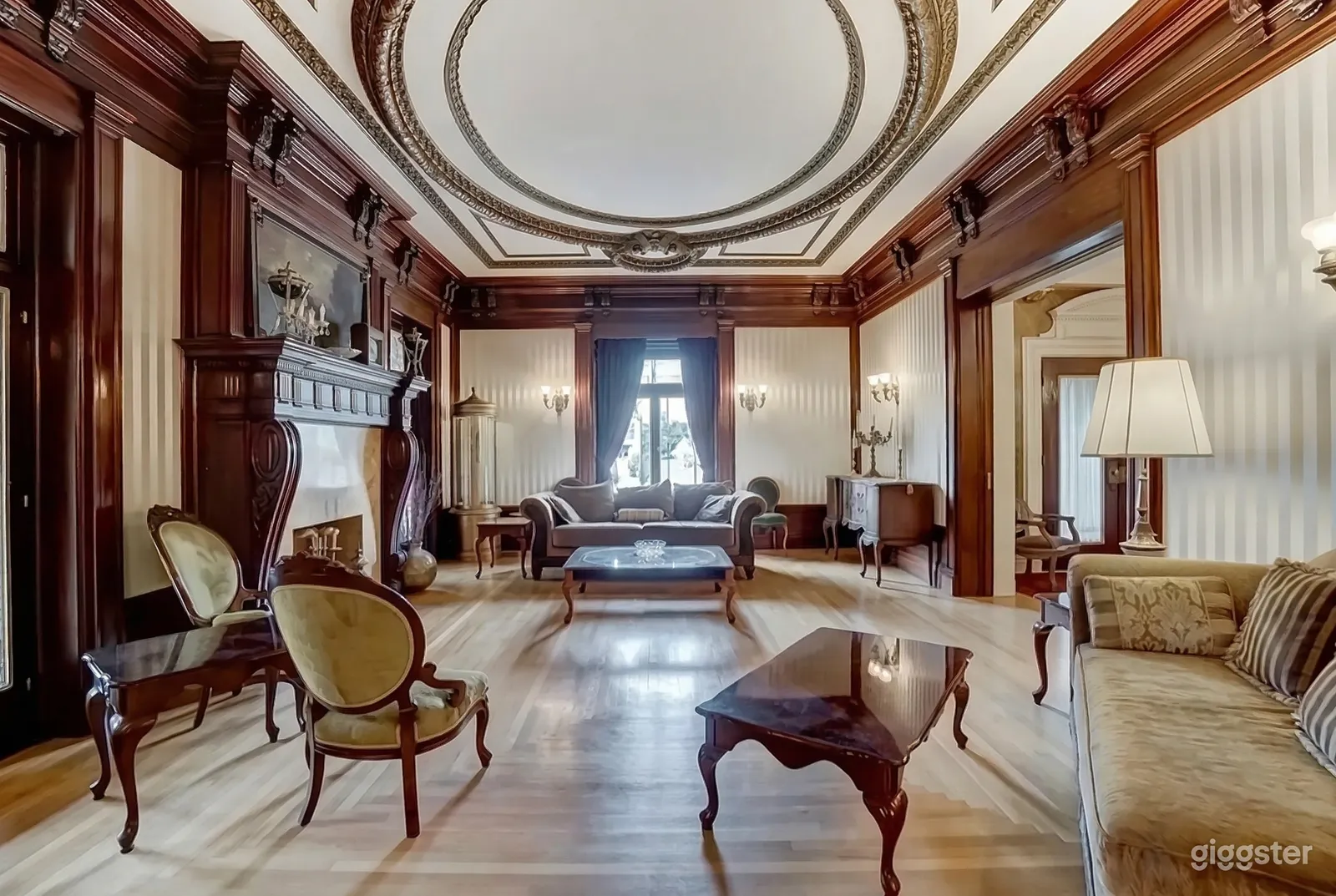 A traditional style room with ornate detailing on the ceiling, carved wooden fireplace mantle, and Victorian furniture.