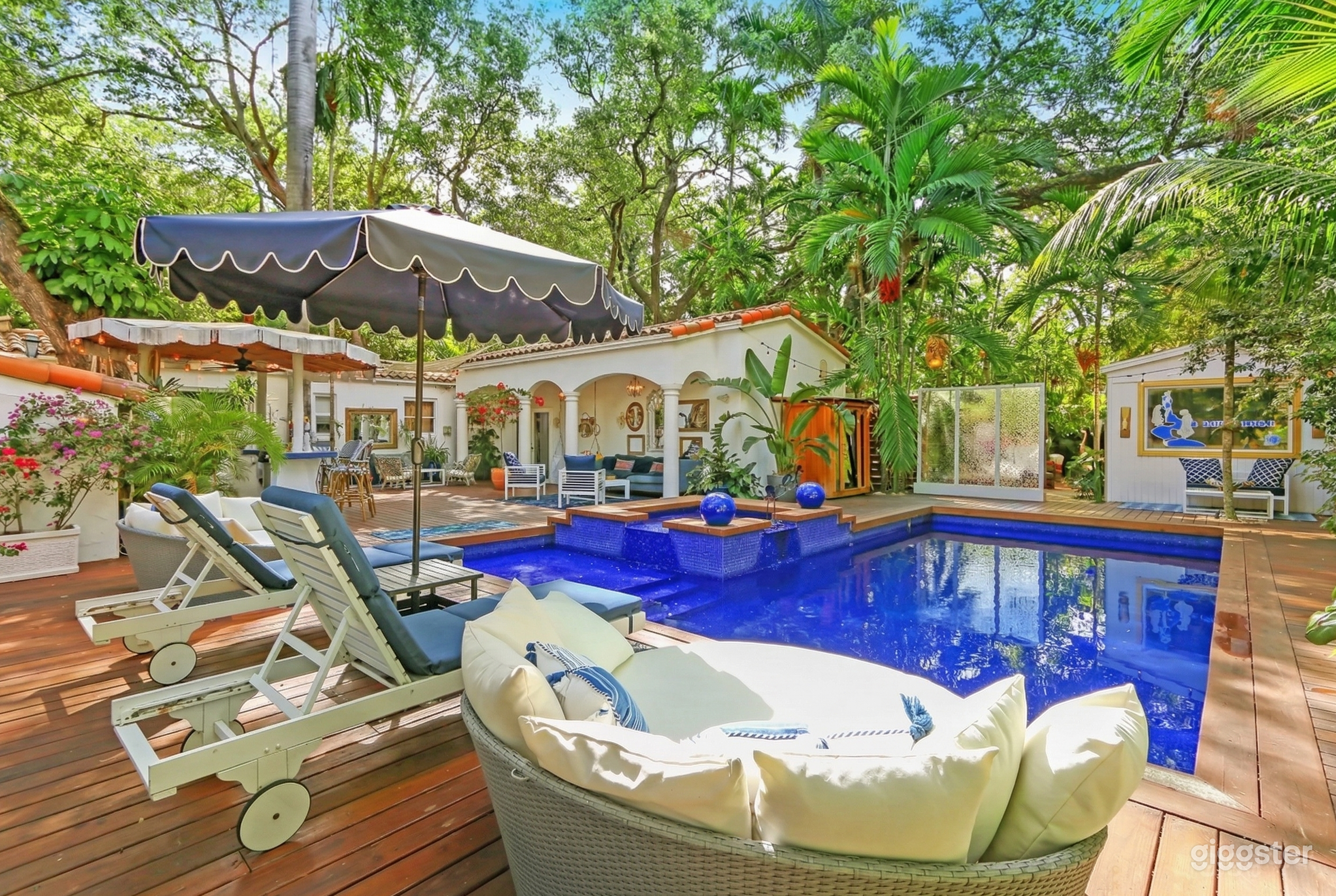 A Spanish style building flanks a bright blue inground pool surrounded by couch and lounge seating.