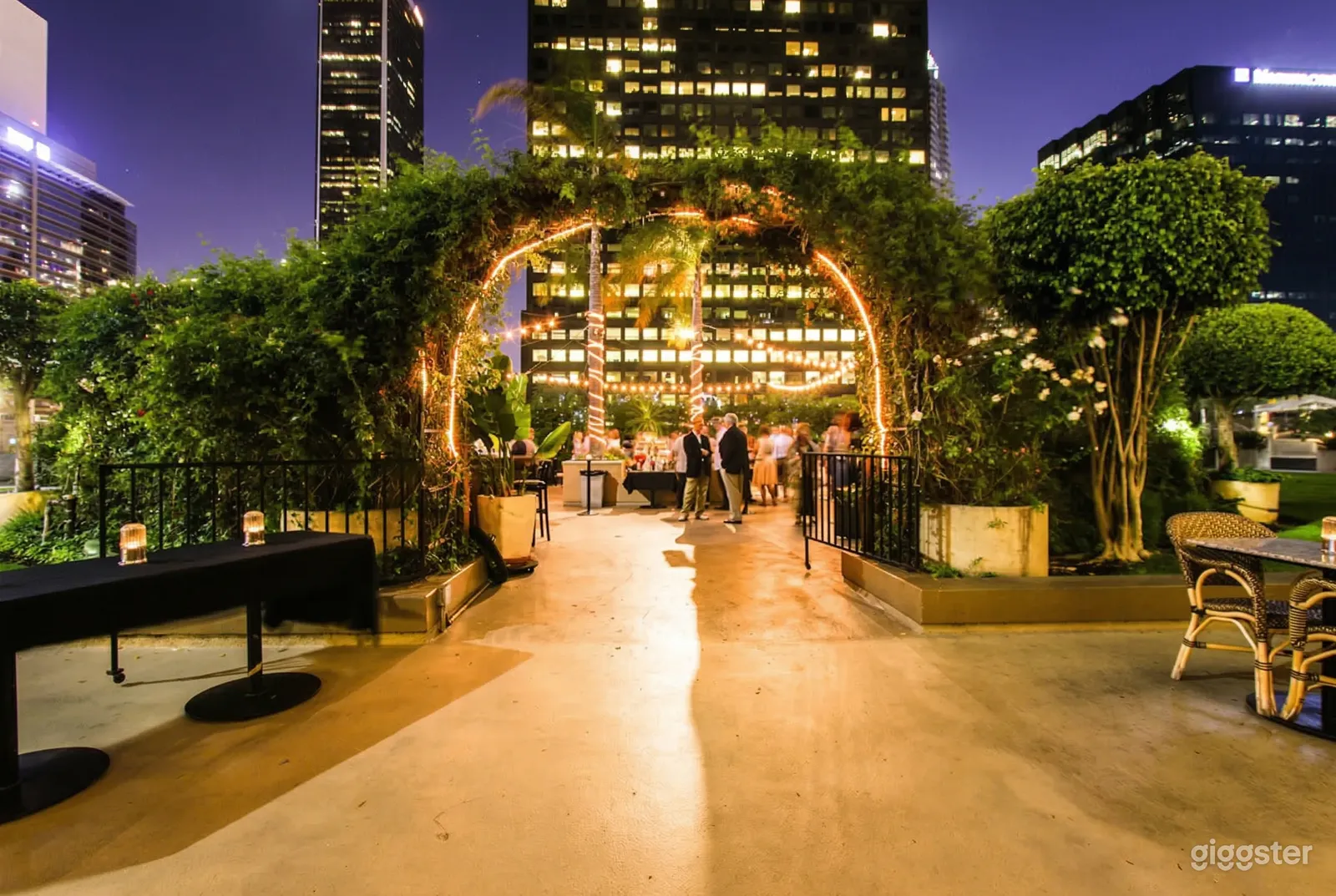 An archway of greenery and lights is the entrance to a summer party venue.