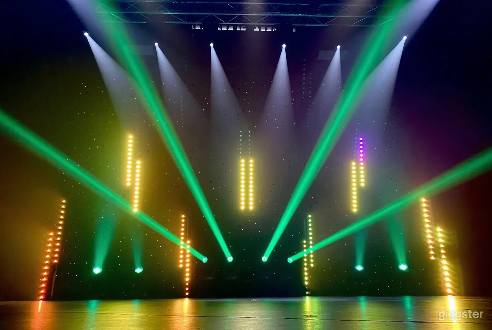 Green and white spotlights shine across an  expansive black wooden stage.