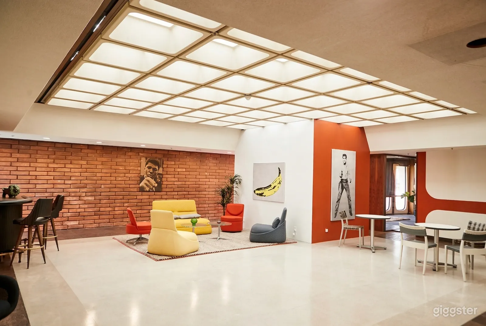 Four colorful chairs sit in a bright room with a windowed ceiling letting in light.