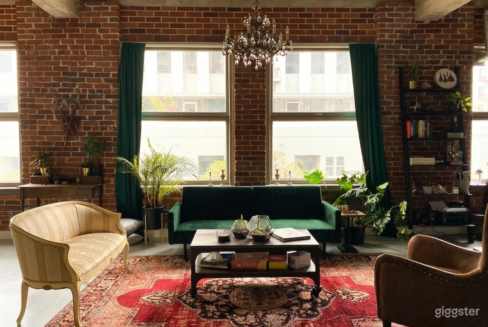 A tapestry rug is centered in a room with a green velvet couch along a windowed brick wall.