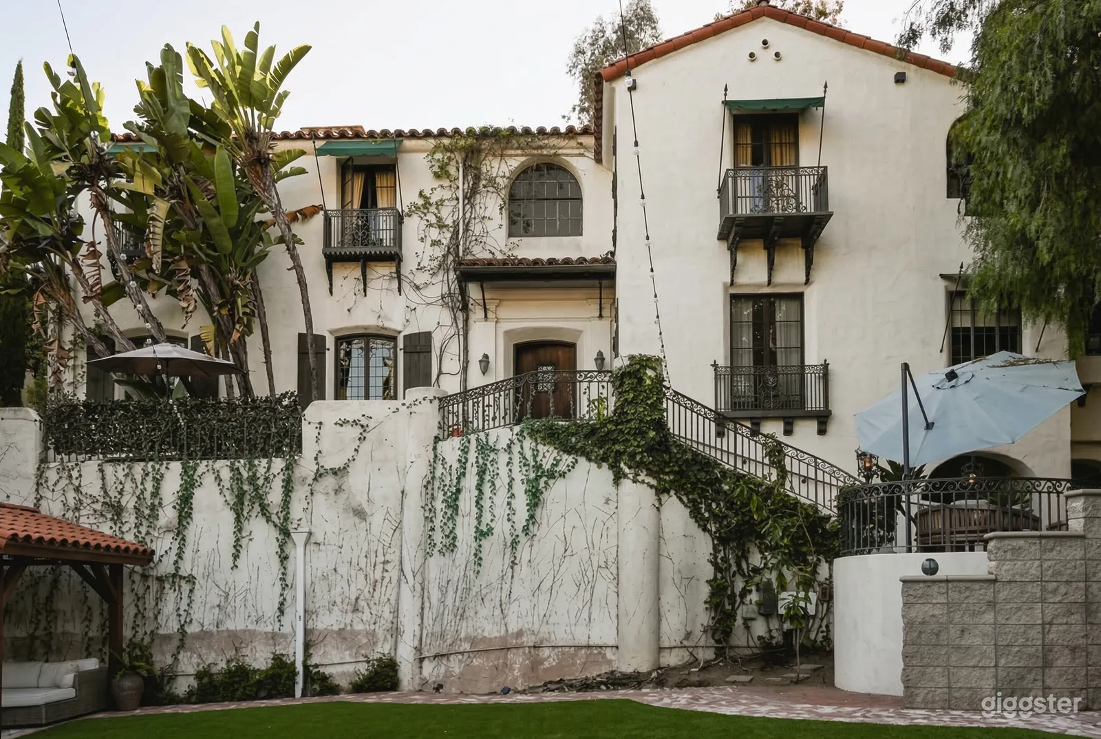 A large stucco mansion overlooks a wall with wrought iron fencing and vines.