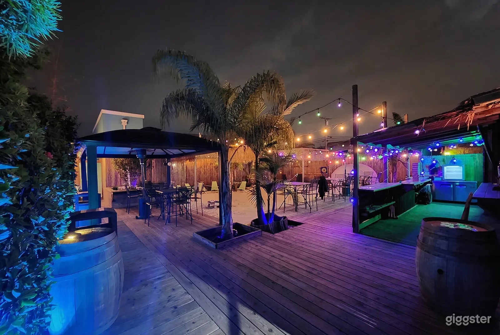 An outdoor party venue is lit up by colorful lighting and has covered as well as open seating areas.