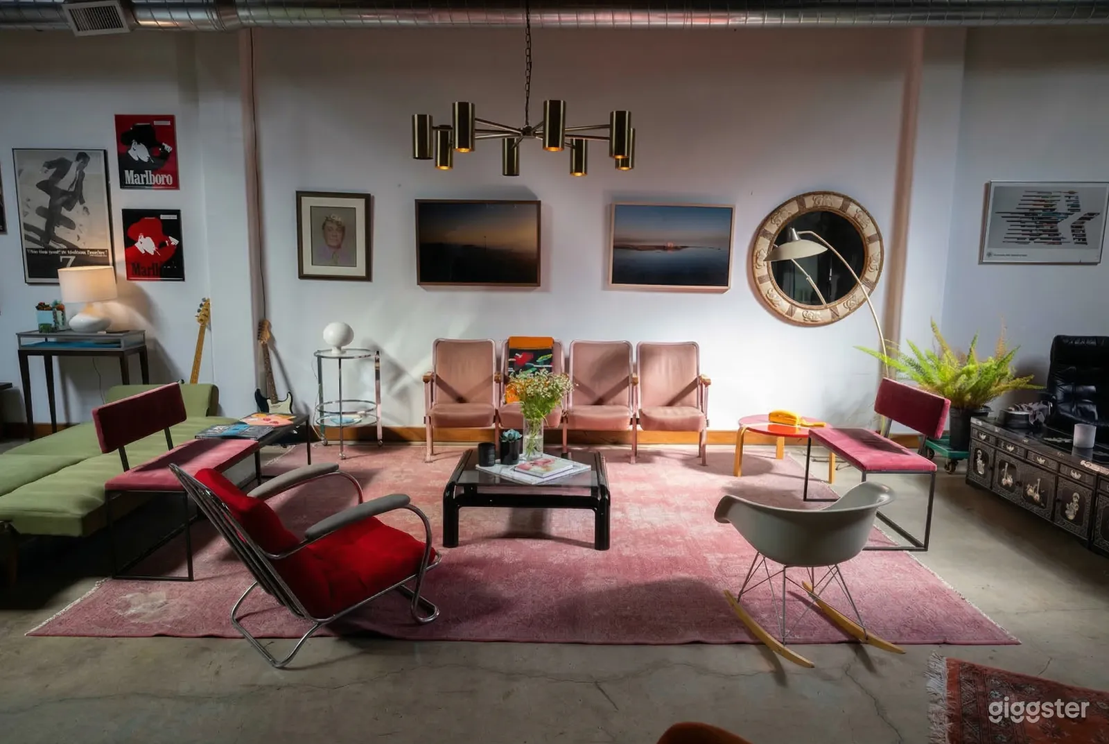 A mid century modern room with pink, green and red seating, a pink carpet, and modern style artwork on the wall.