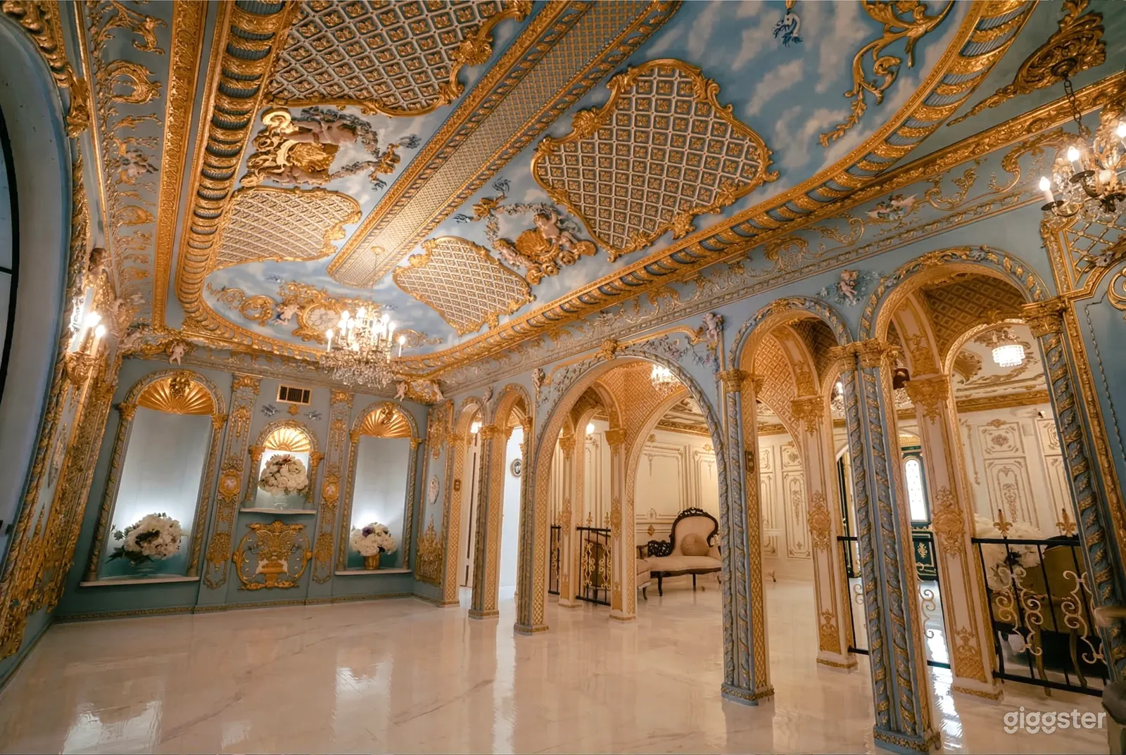 A ballroom style room with pillars and an ornate gold and grey ceiling.