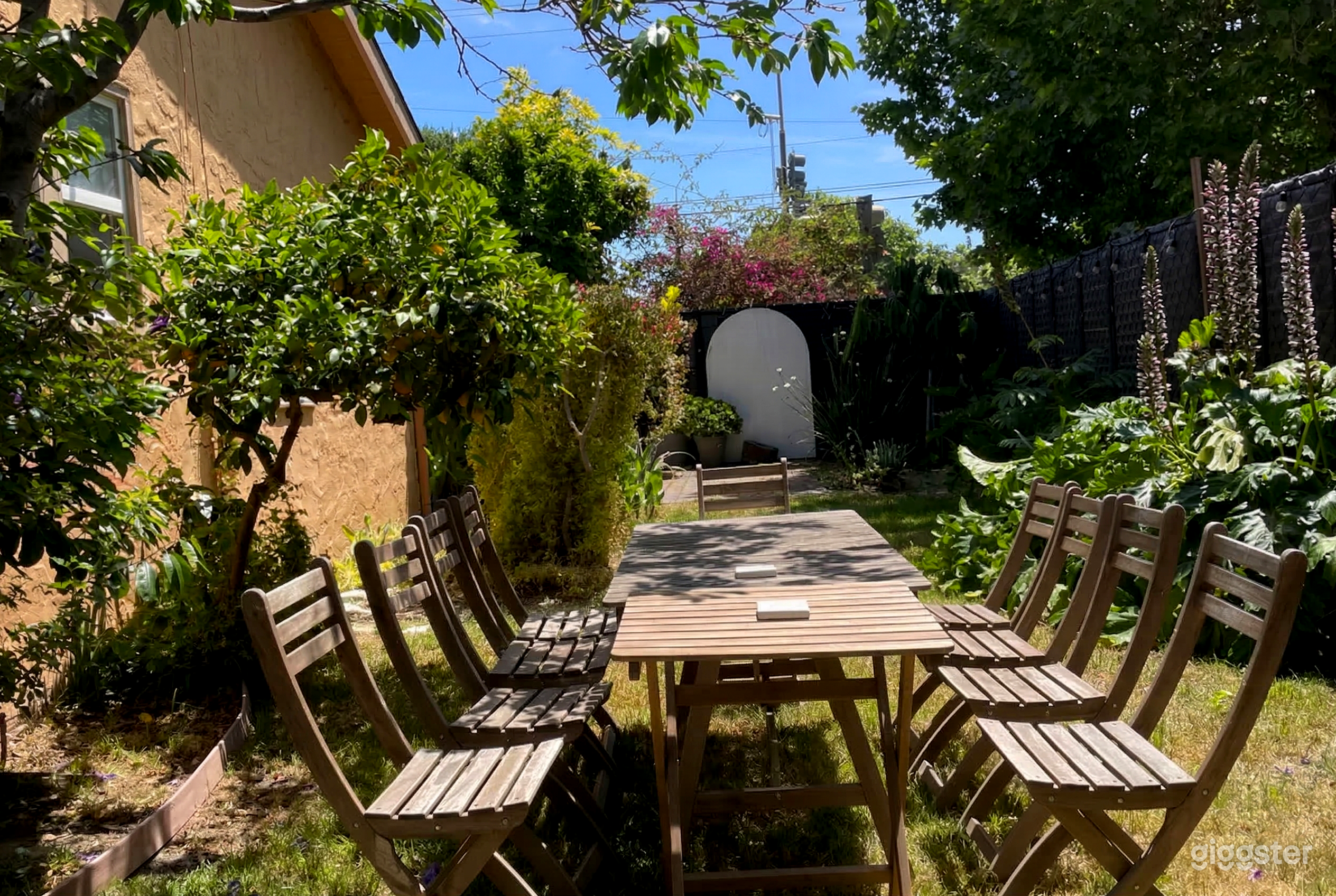 Two tables with chairs are central in a fenced backyard surrounded by succulents and trees.