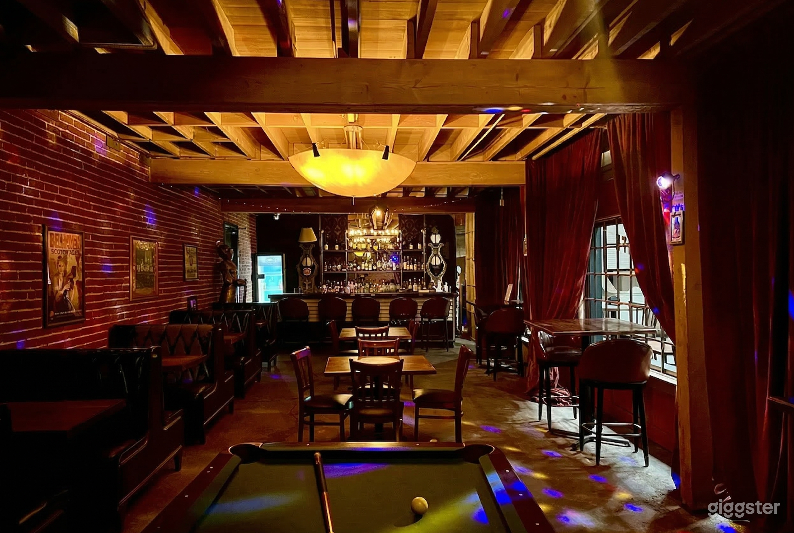 A cozy bar with booth and table seating as well as a pool table and lit up bar area.