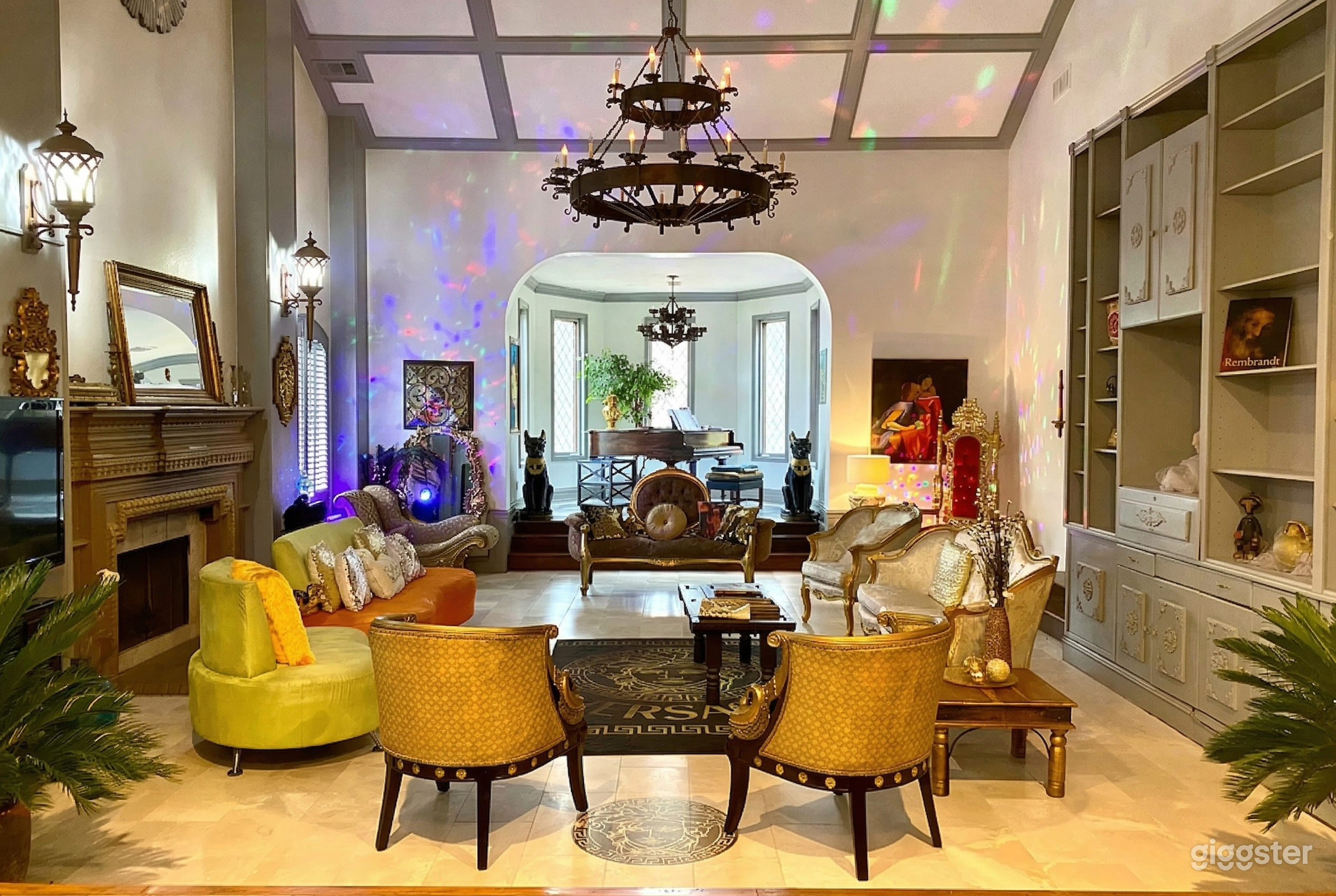 Victorian style furniture sits in a circle in front of a fireplace and a piano sits behind them.