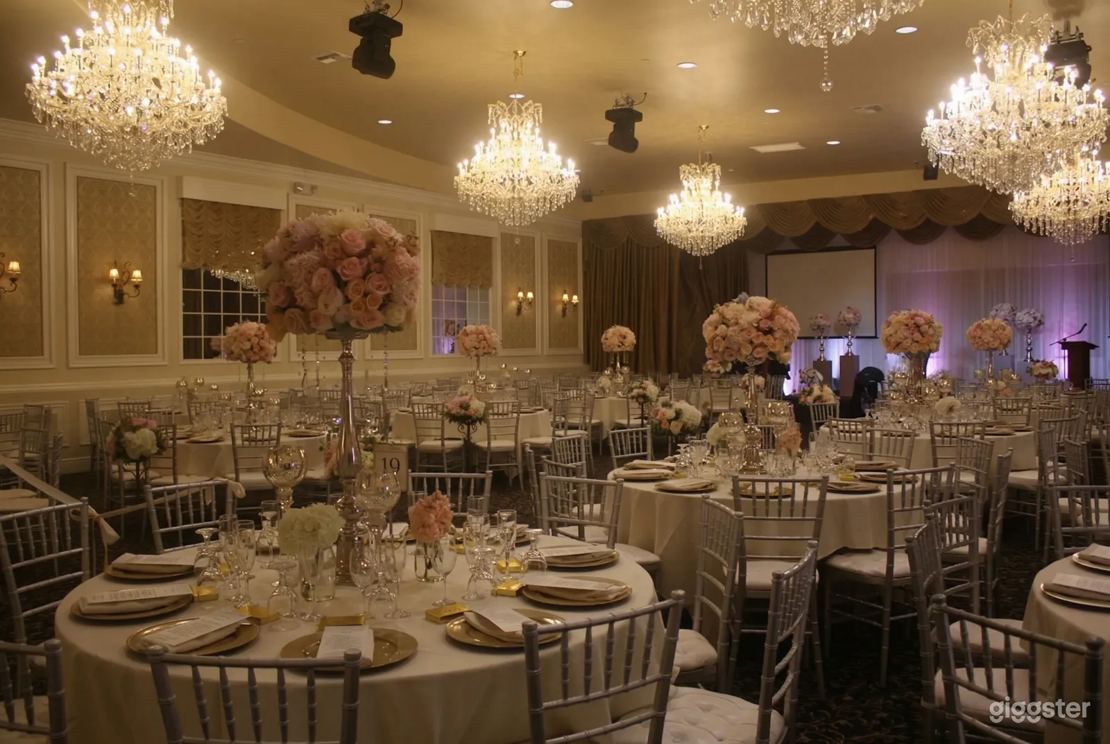 Glass chandeliers hang over round tables decorated with floral topiaries in a hotel banquet room.