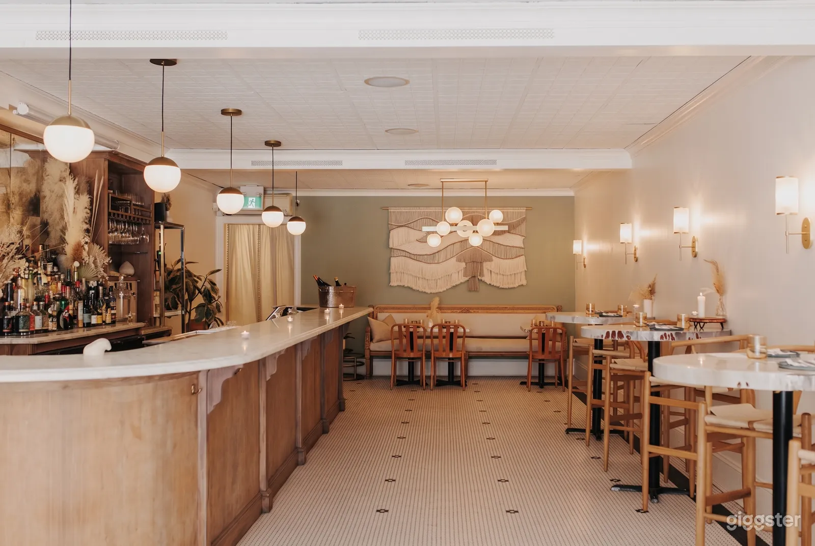 A cafe bar has beige decor, a bar on one side and cafe style tables on the other side as well as bench seating at the back.