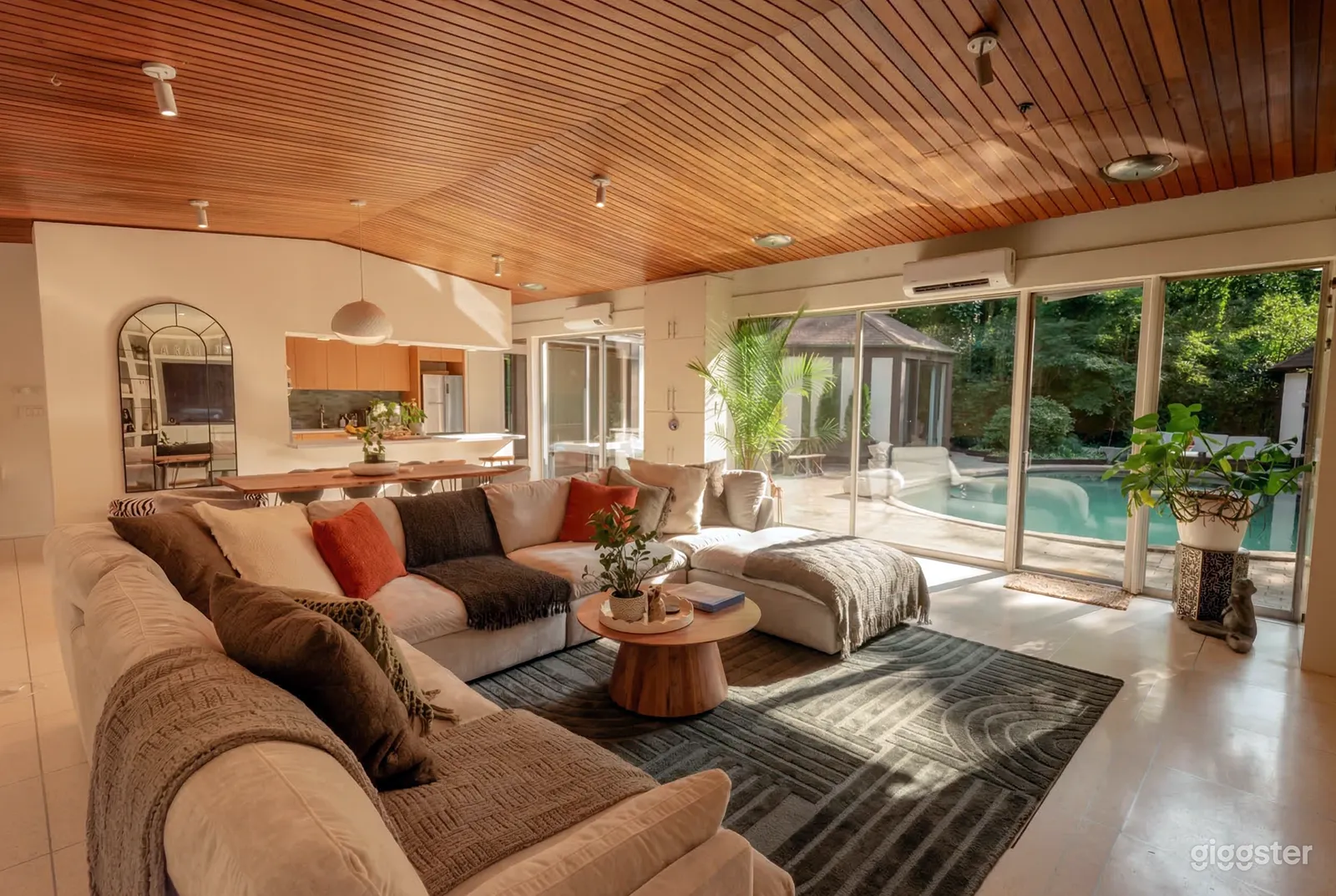 A room with a large sectional couch overlooks an outdoor swimming pool and deck area.