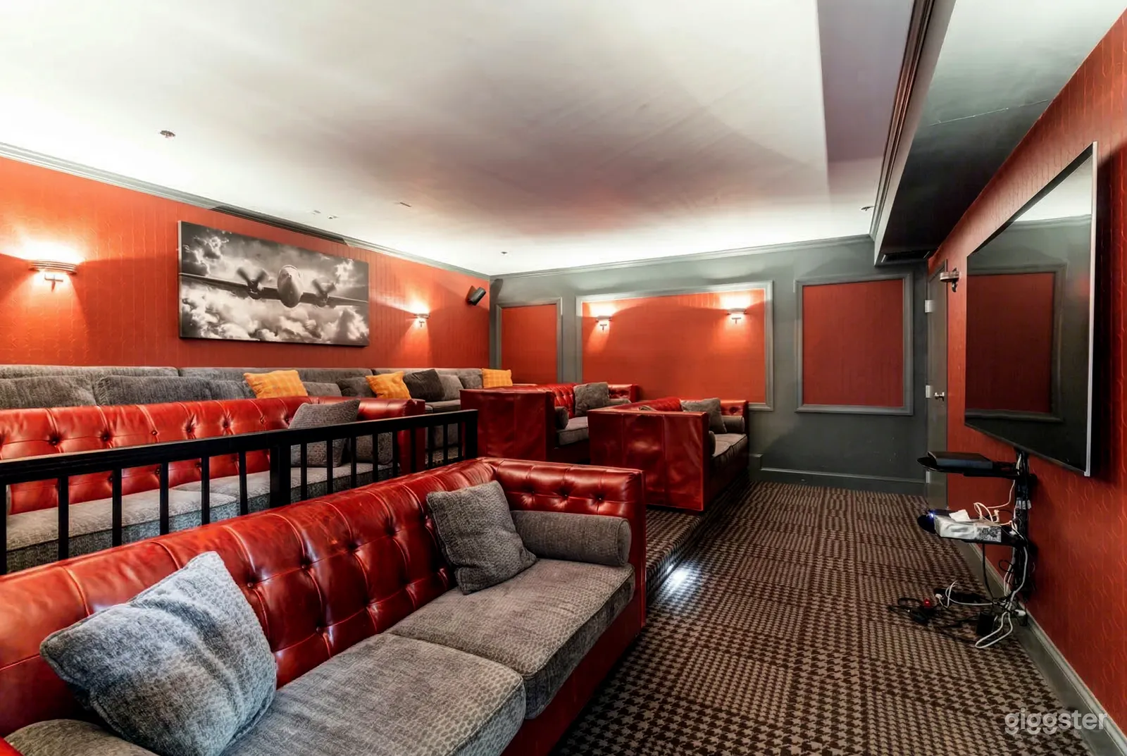 Long grey and red couches face a small cinema screen on a wall.