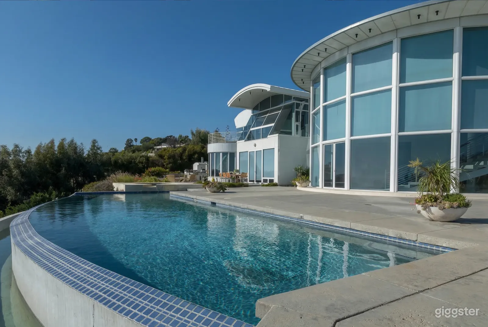 A circular shaped modern hilltop mansion faces a large inground pool.