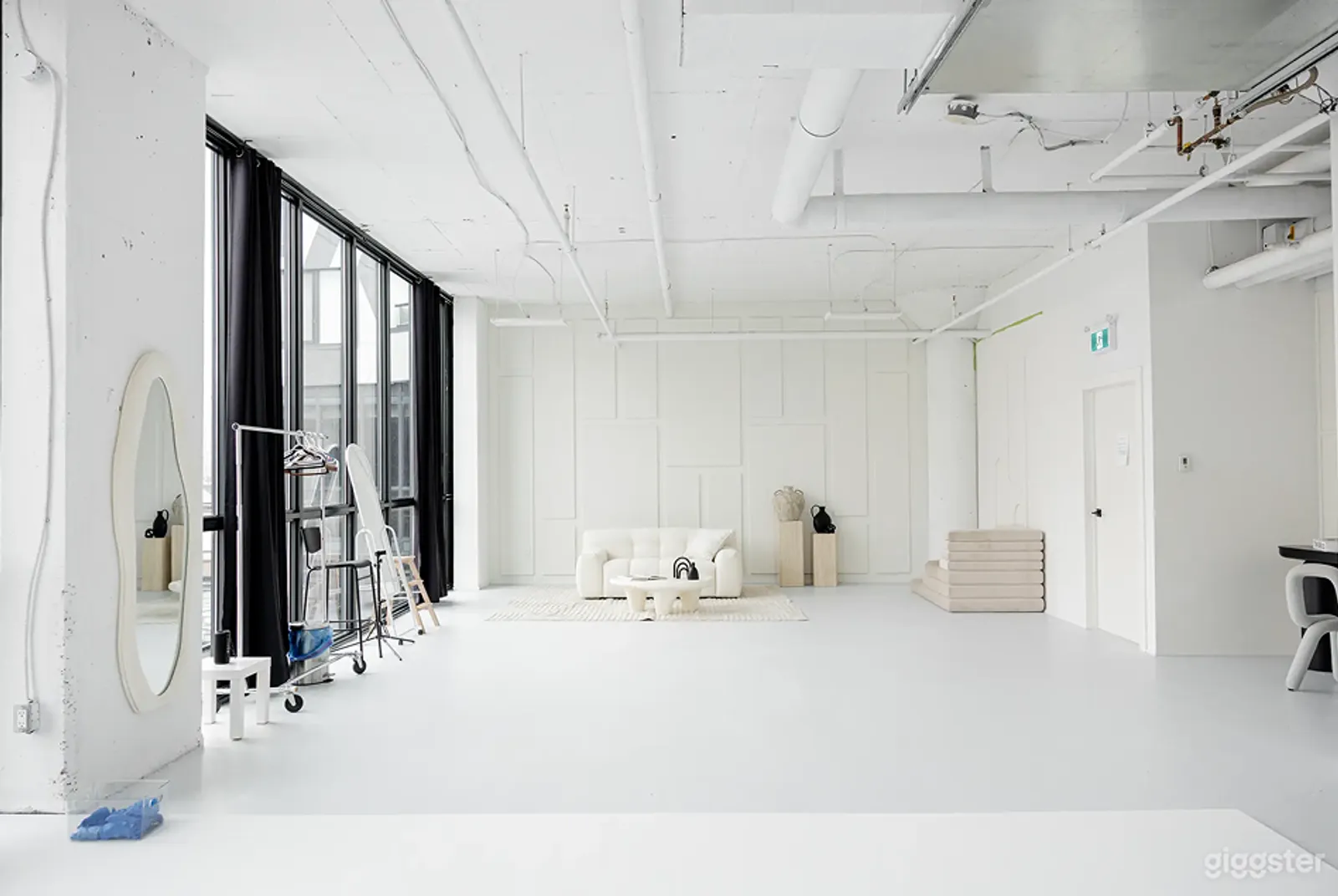 An industrial style room is painted white from floor to walls to ceiling, with tall windows on one wall and a white couch and table at the end.