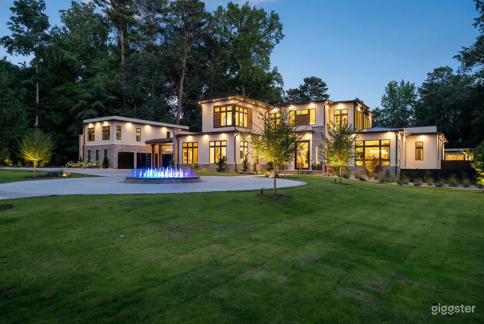 A multi-windowed well lit mansion overlooks a fountain and expansive lawn.