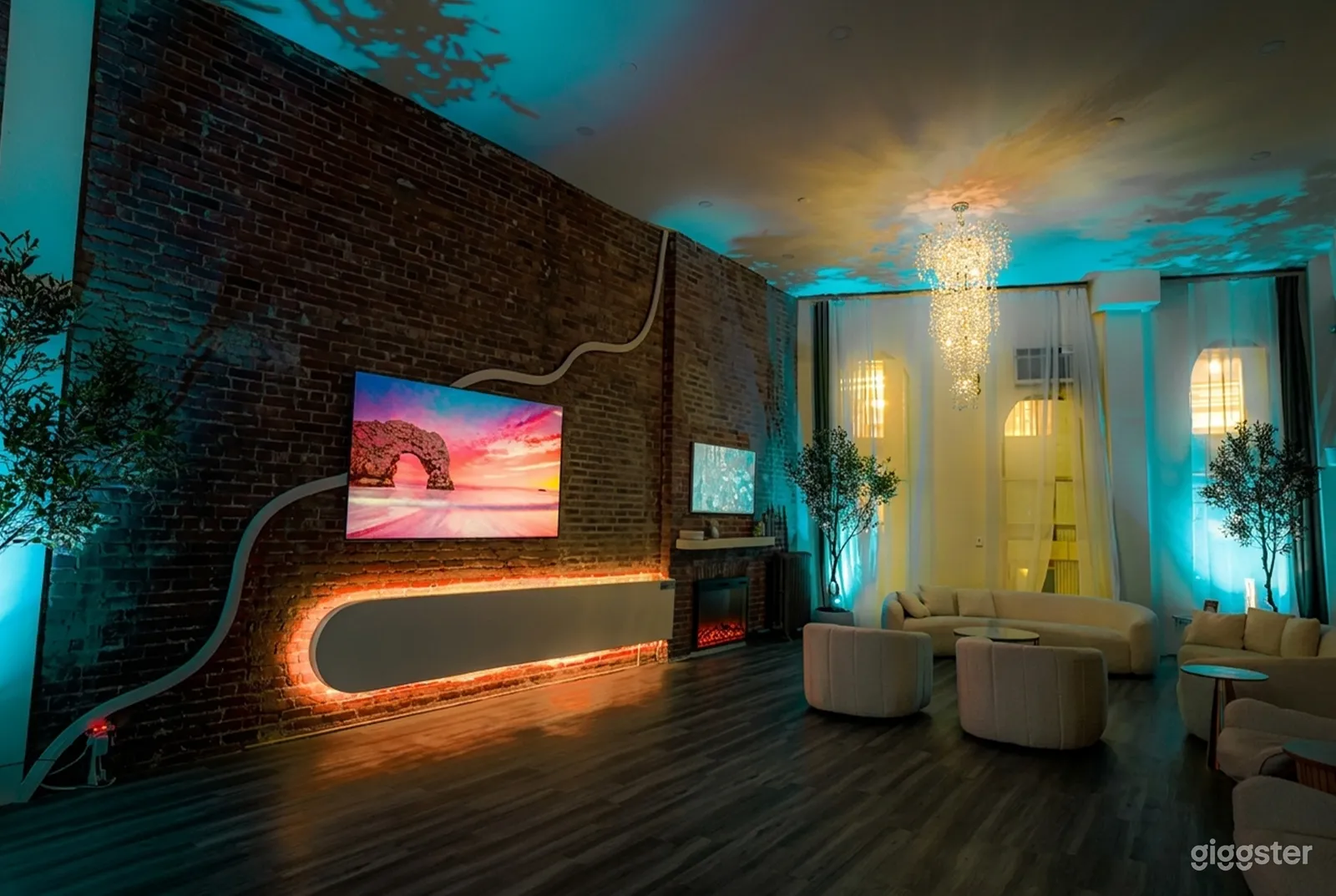 A television highlights the wall in a mid-century modern room with blue lighting and beige couches off to the side.