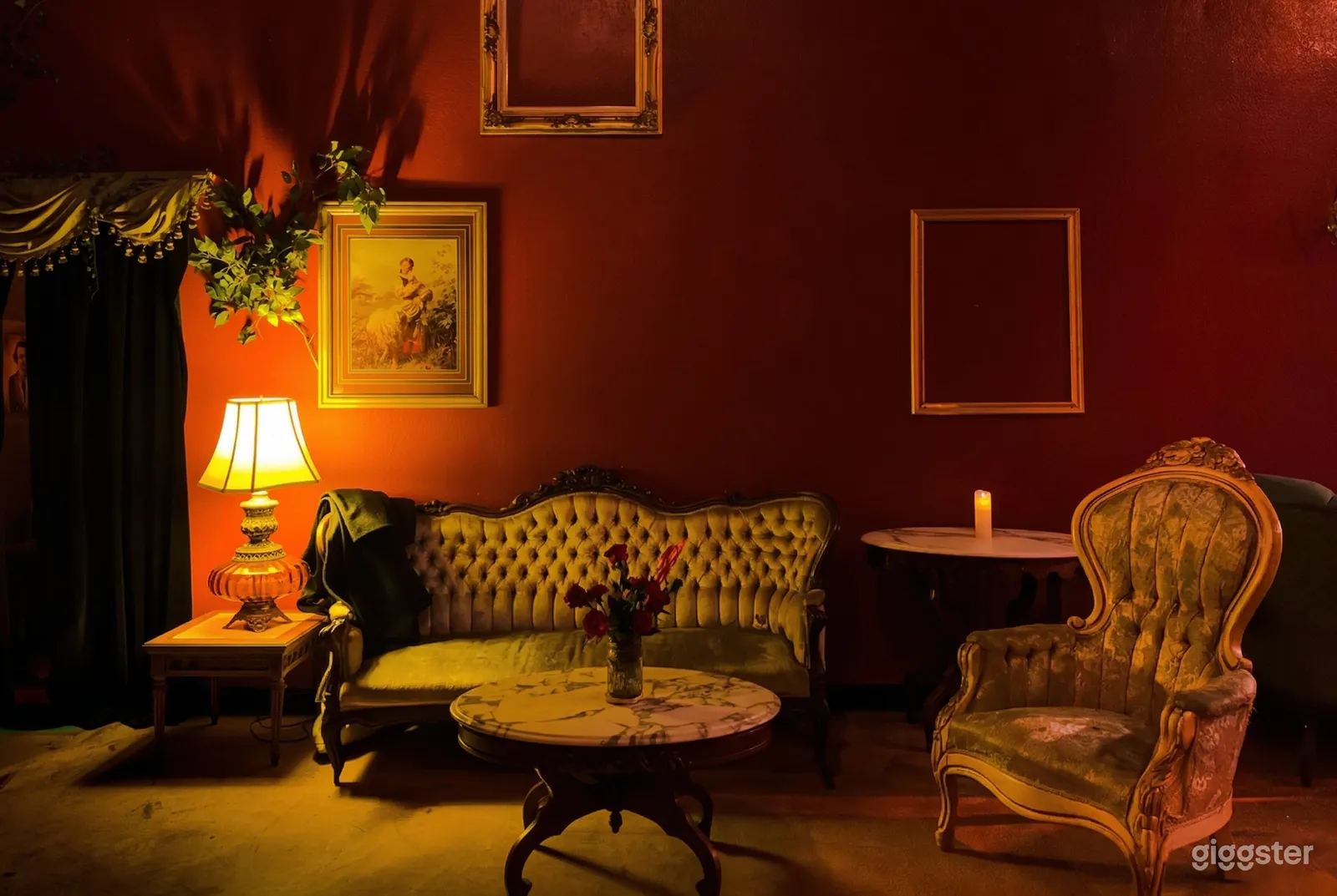 A gold colored vintage couch, chair, tables and lamp sit in front of a wall painted red.
