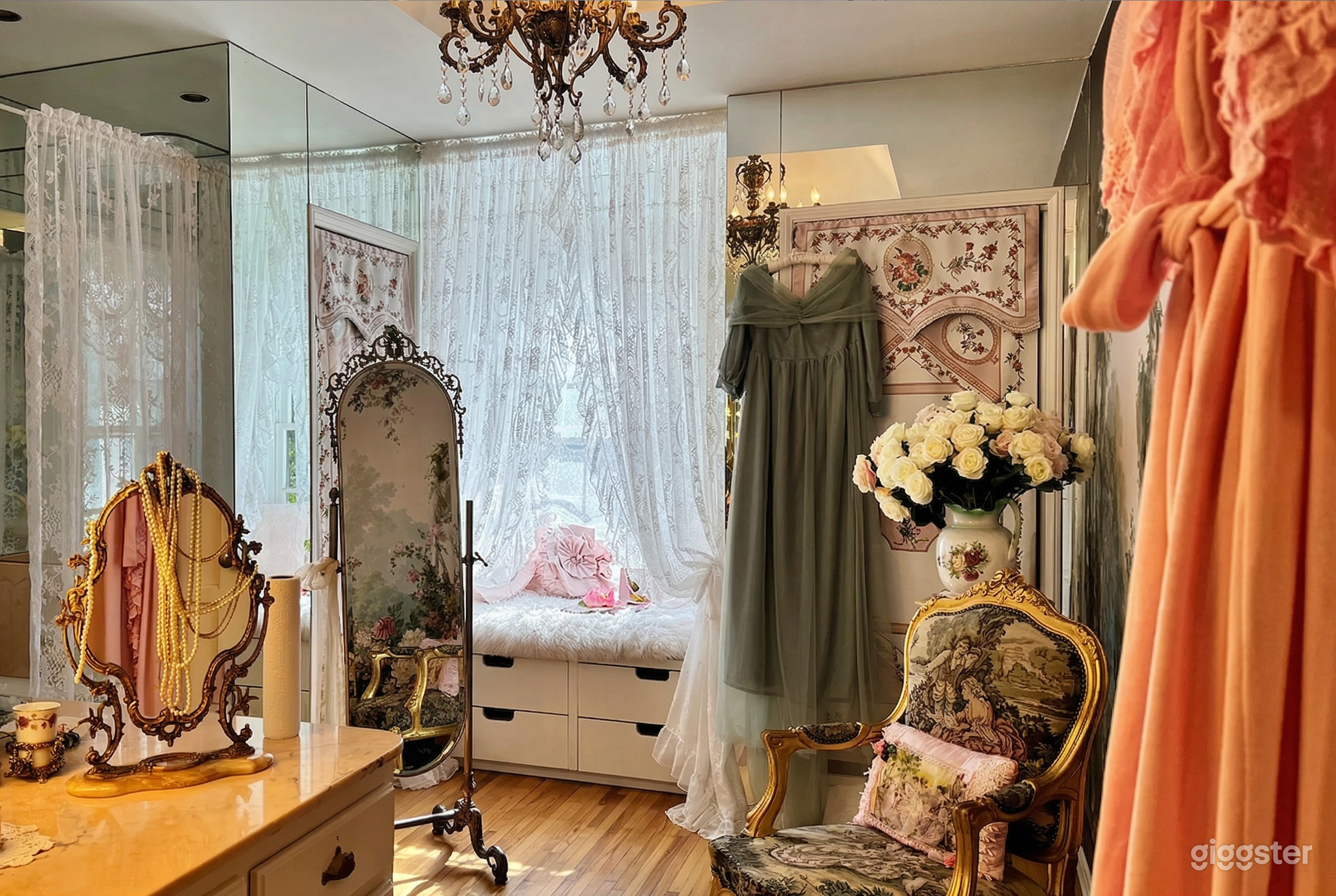 A dressing room has curtains, mirrors, necklaces and dresses, all vintage style.