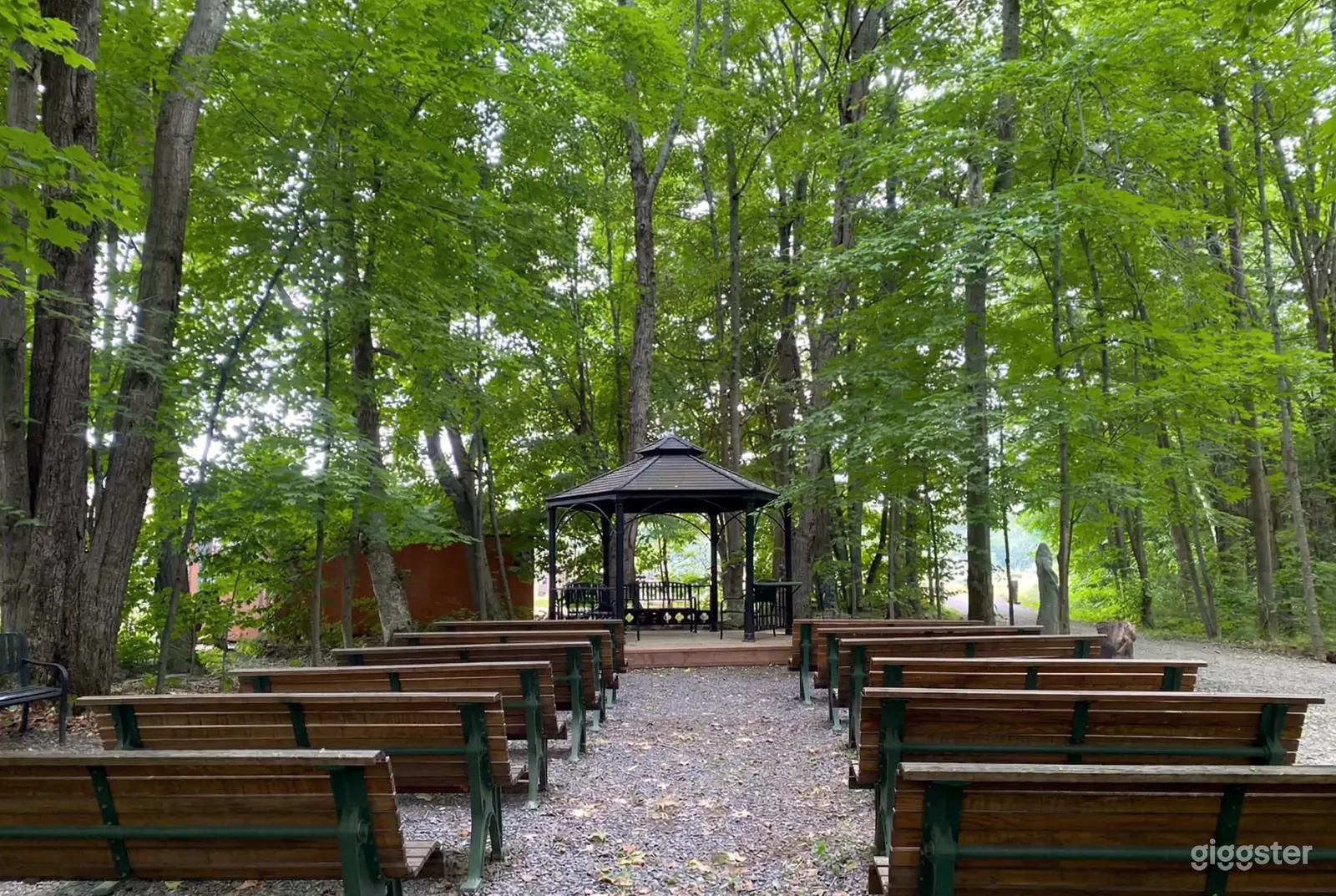 Rows of benches face a pergola in a wooded area.