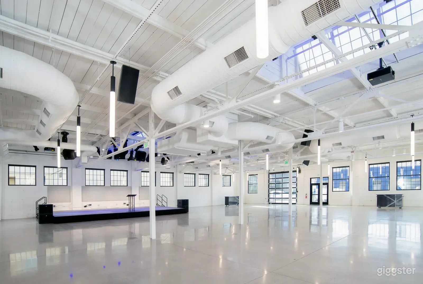 A large, white industrial type space has visible big pipes and iron supports in the ceiling.