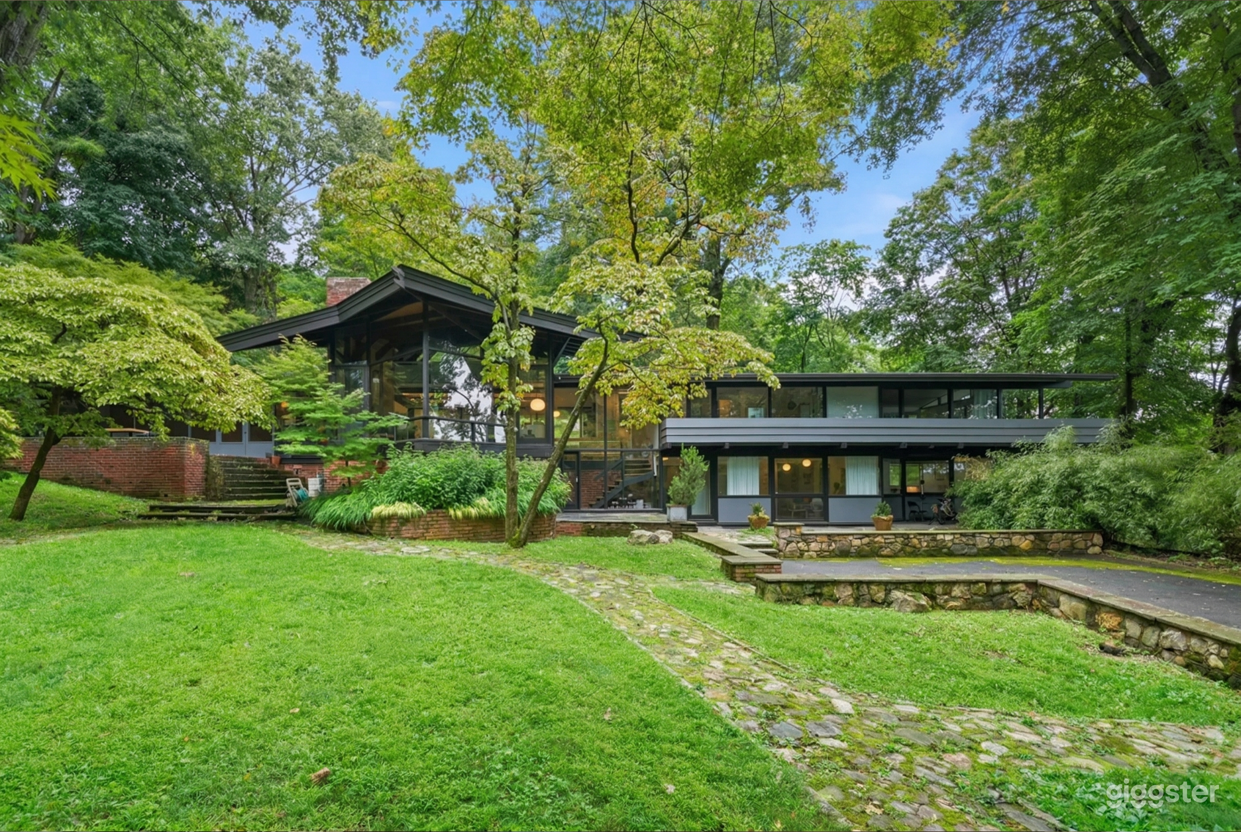A large modern home with many windows faces a grassy property with a mowed lawn, patio, and tall trees.