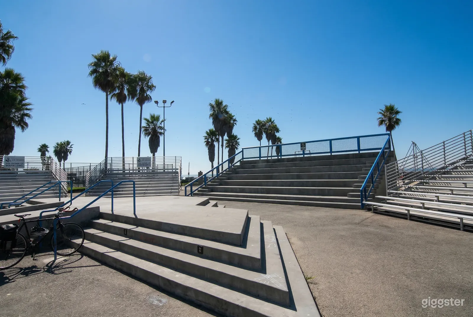 Palm trees surround an outdoor event area with multiple sets of long bleacher seating.