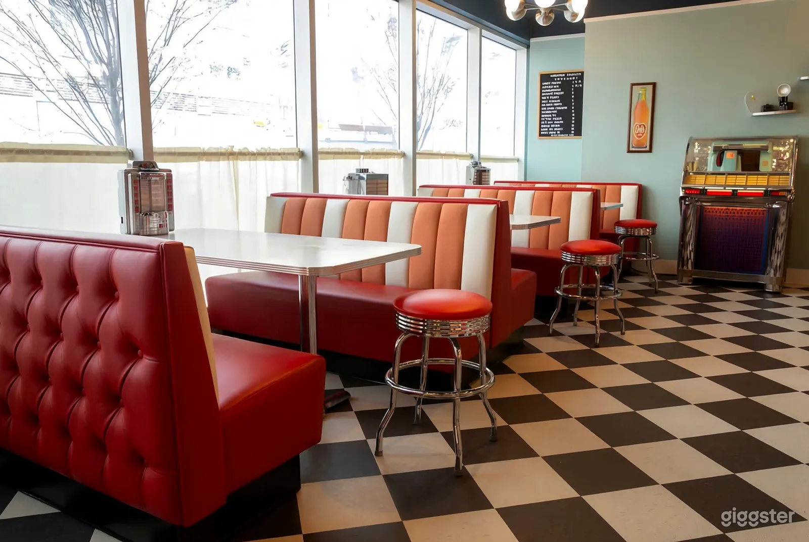 Booth seating of white, orange and red lines the window of a diner with checkered floors.