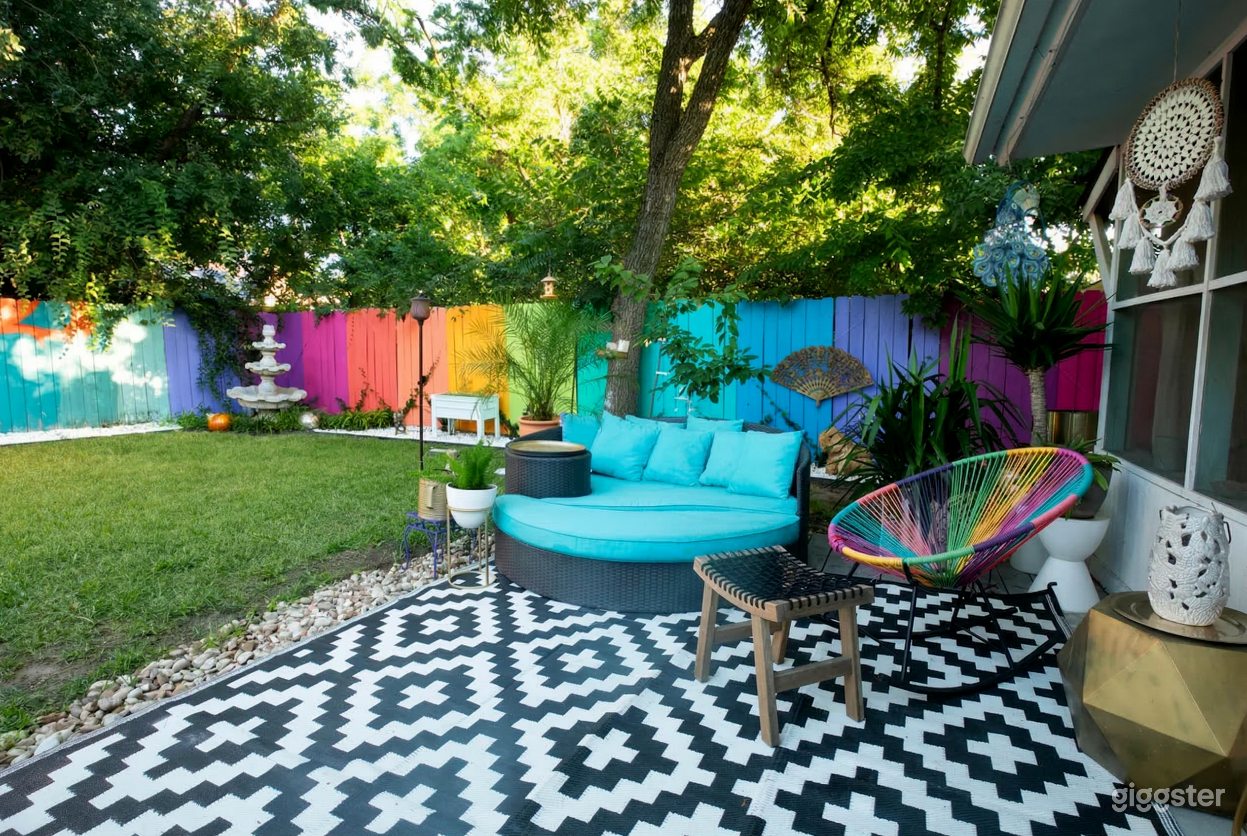 A multicolored fence surrounds a backyard space with a turquoise lounge couch and rainbow wicker chair.