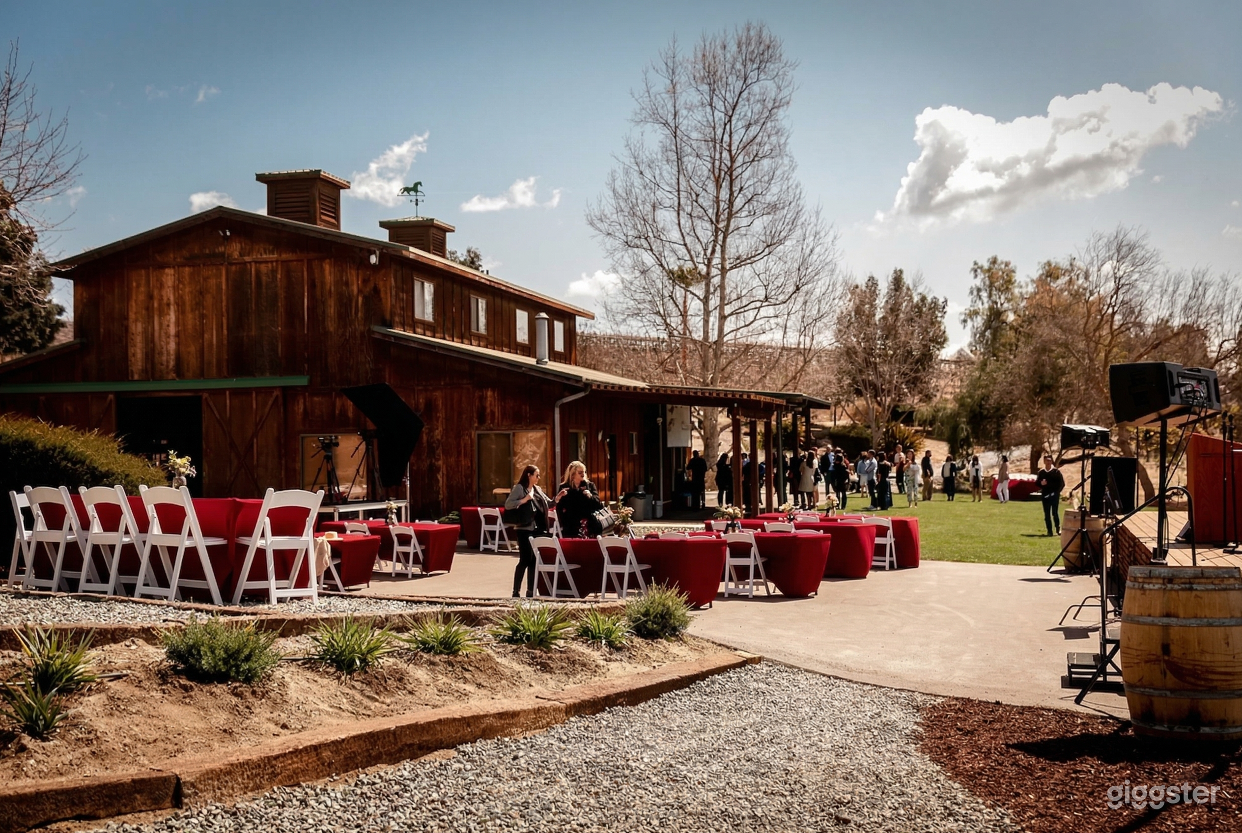 Tables and chairs sit in front of a stage area with a barn event building behind them.