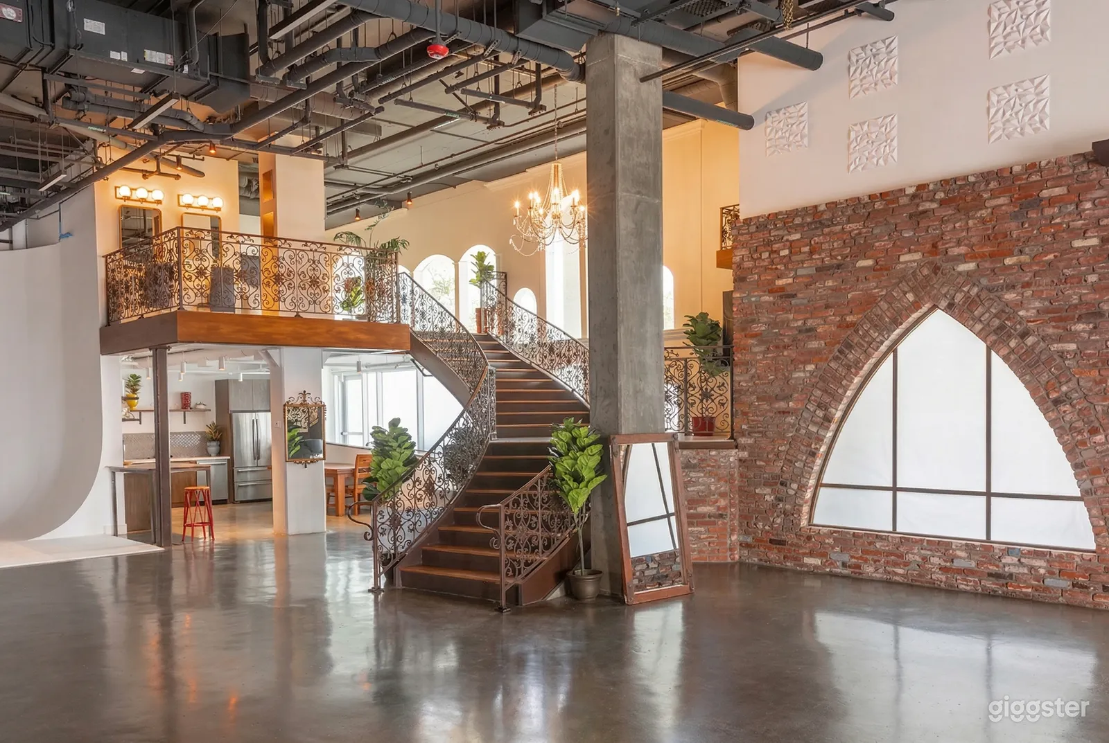 A large studio has a brick wall, a winding ornate staircase, and a shiny floor. 