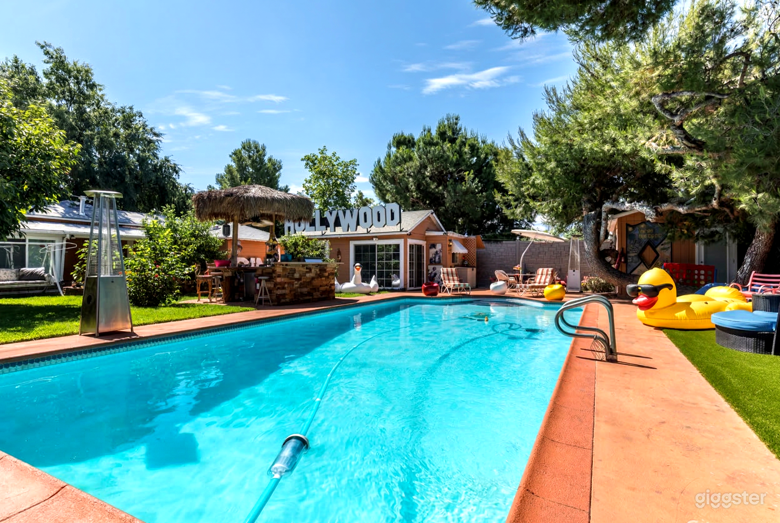 Pool toys and a cabana with a Hollywood sign invite guests to a large inground pool.