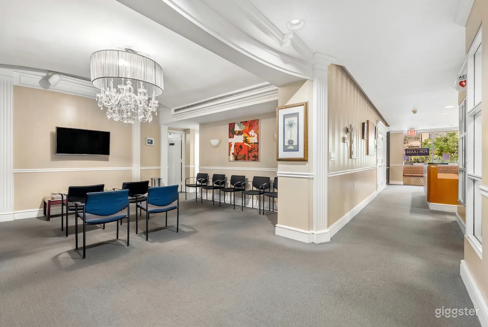 A waiting room is filled with blue and black chairs, and sits beside a reception hallway.