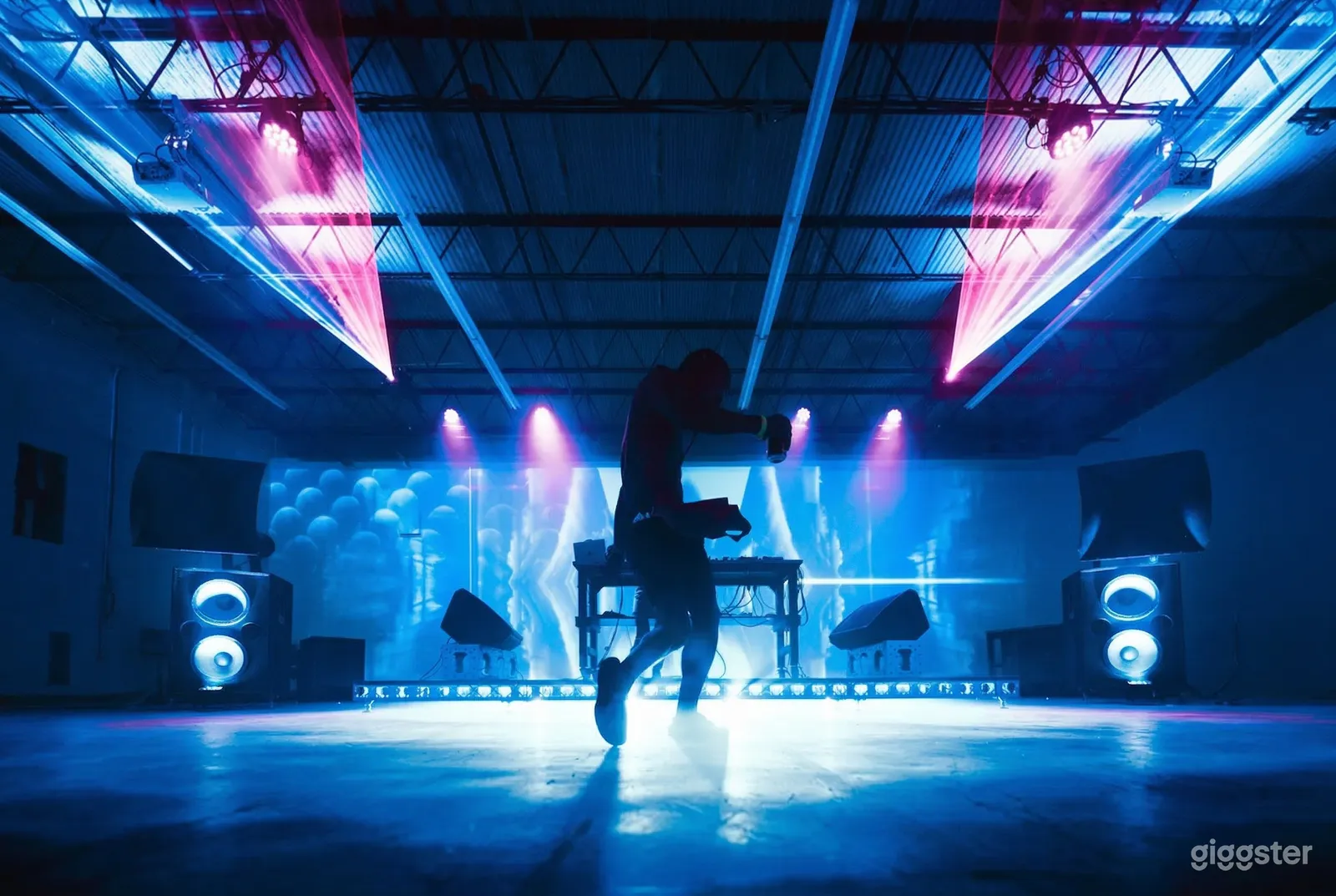 A lone person dances in front of a sound stand in an event room with blue lighting and pink spotlights.