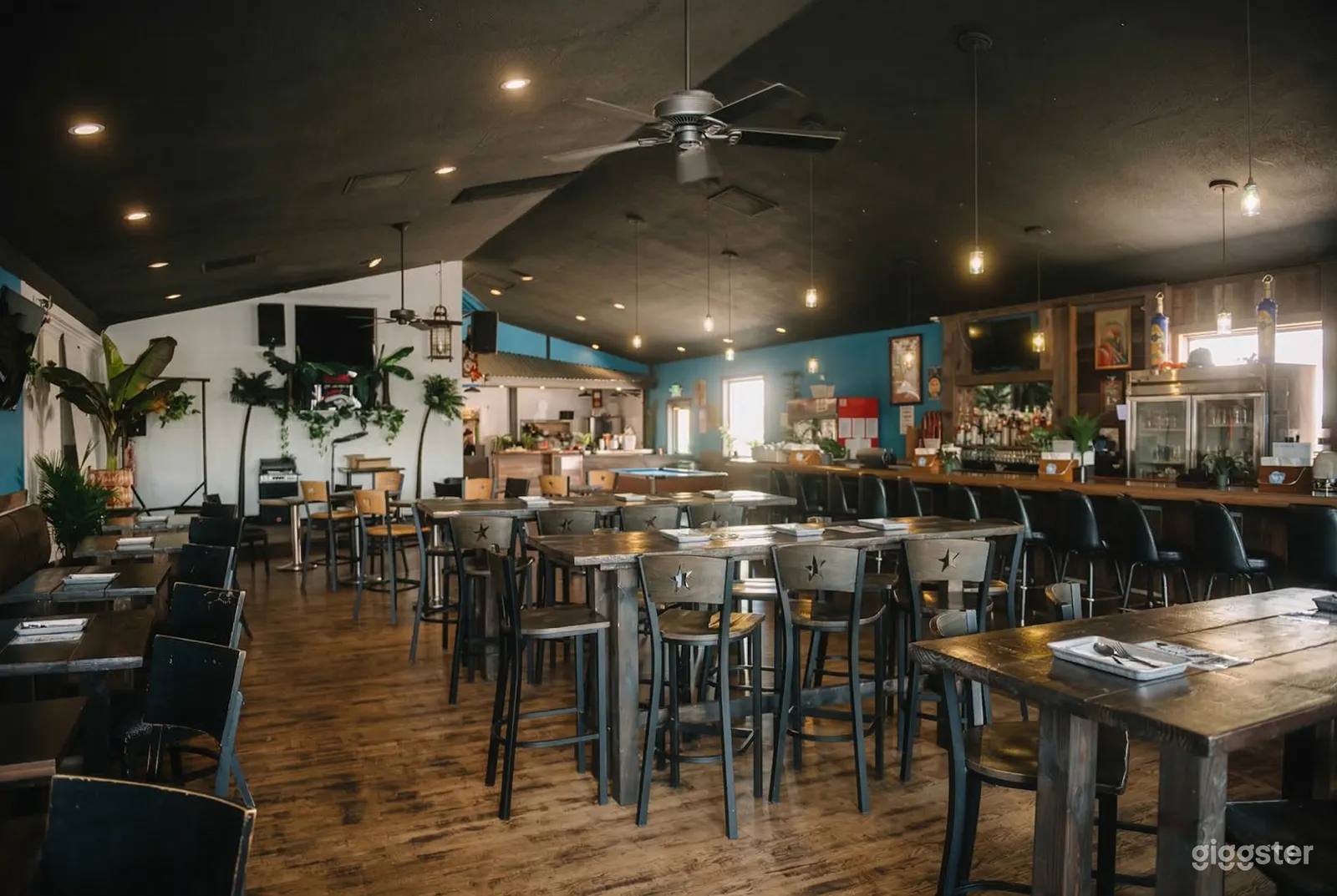 Long tables with multiple chairs are in front of a bar with seating and dim lighting.