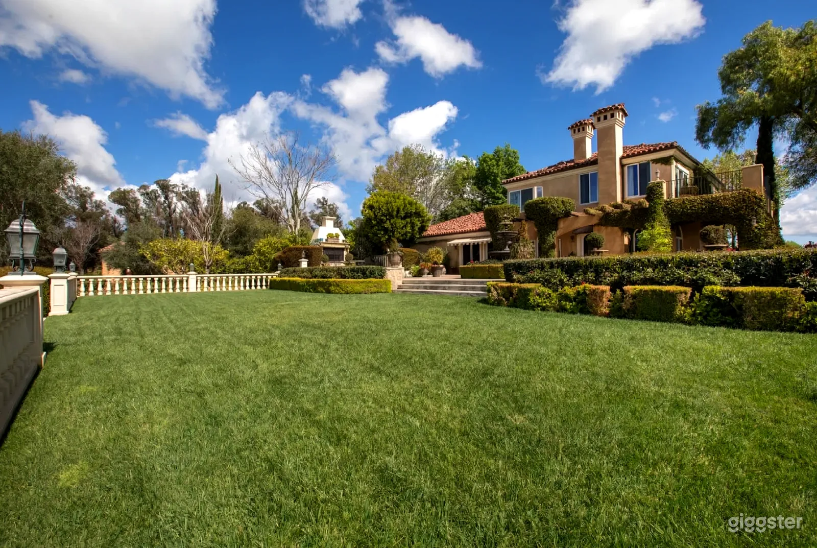 A large lawn flanks an estate style home surrounded by hedges and trees.