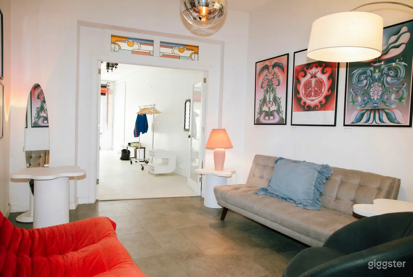 A modern room with a colorful artwork and seating opens into a large empty room with a coat rack.