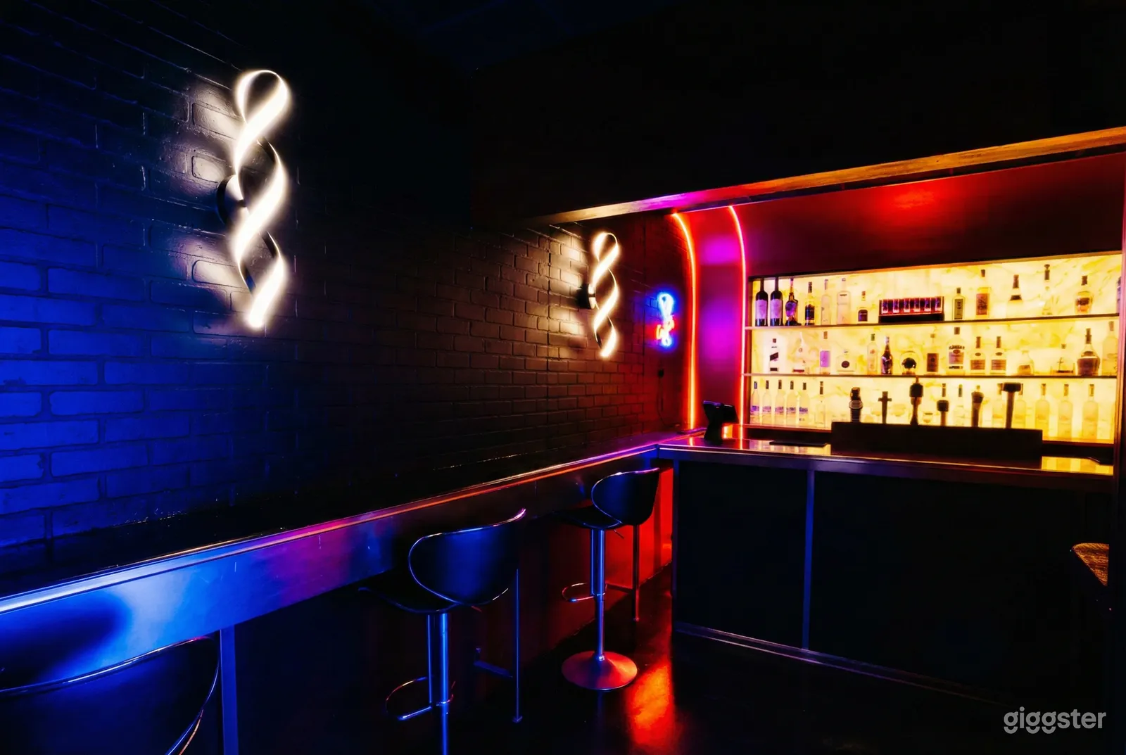 Neon lights and wall sconces light up a bar venue with a brightly lit bar setup as the focal point.