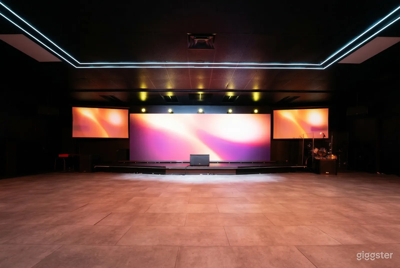 Large electronic screens sit on either side of a massive screen facing an empty exposition floor.