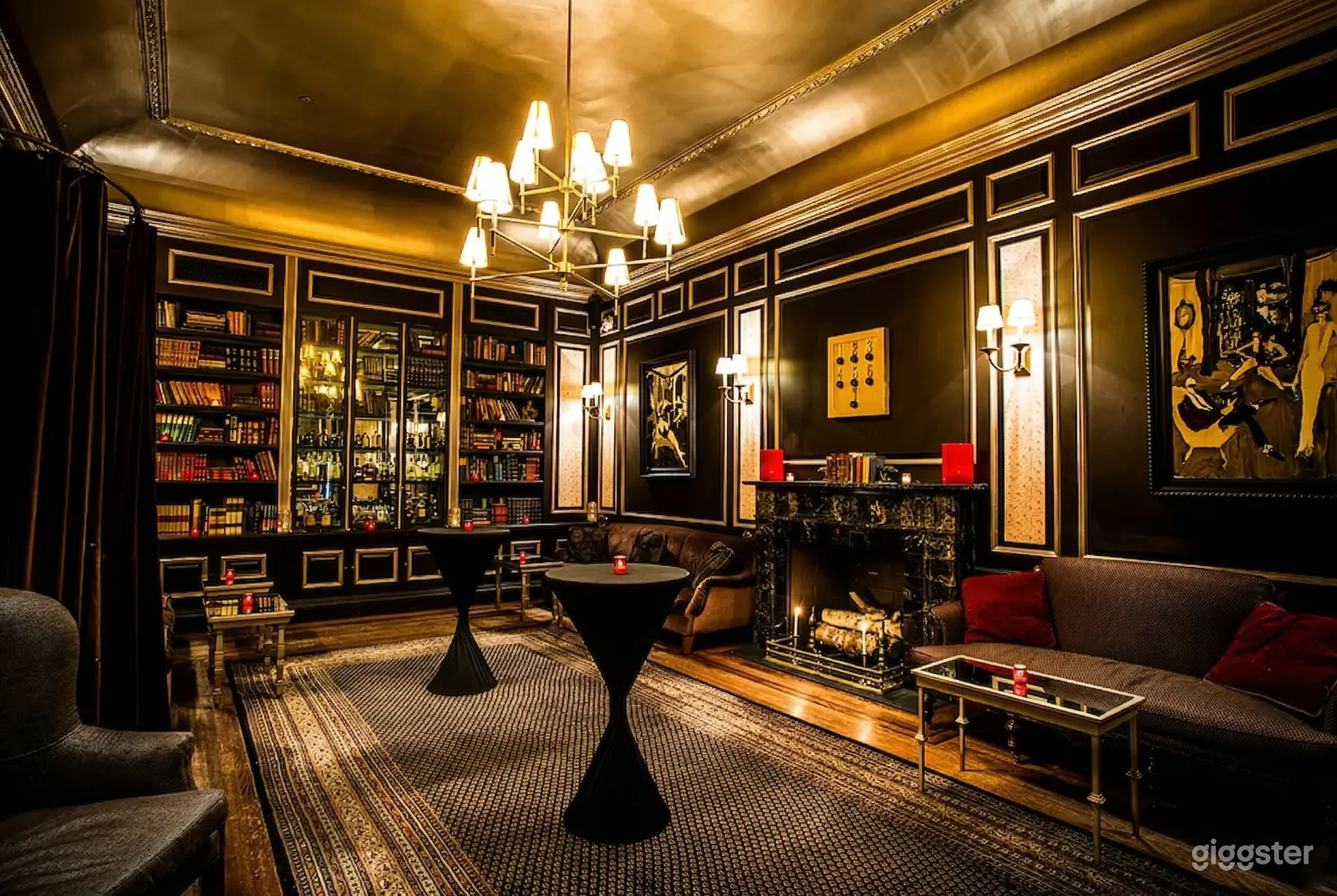 A vintage decor room with a full-walled bookshelf, ornate fireplace, black occasion tables and wall sconce lighting.