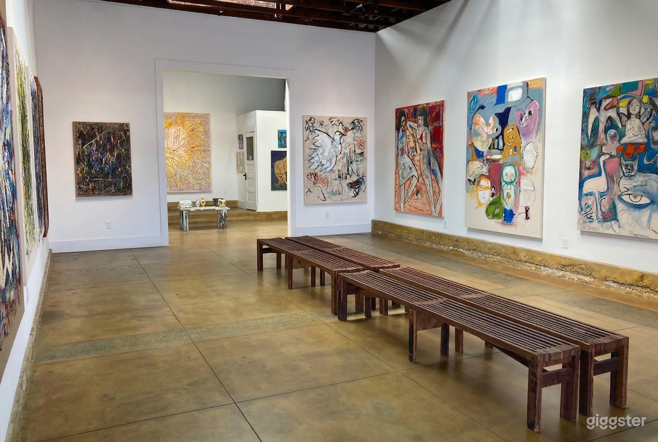 Long wooden benches are central in a gallery space with large colorful paintings on the walls.