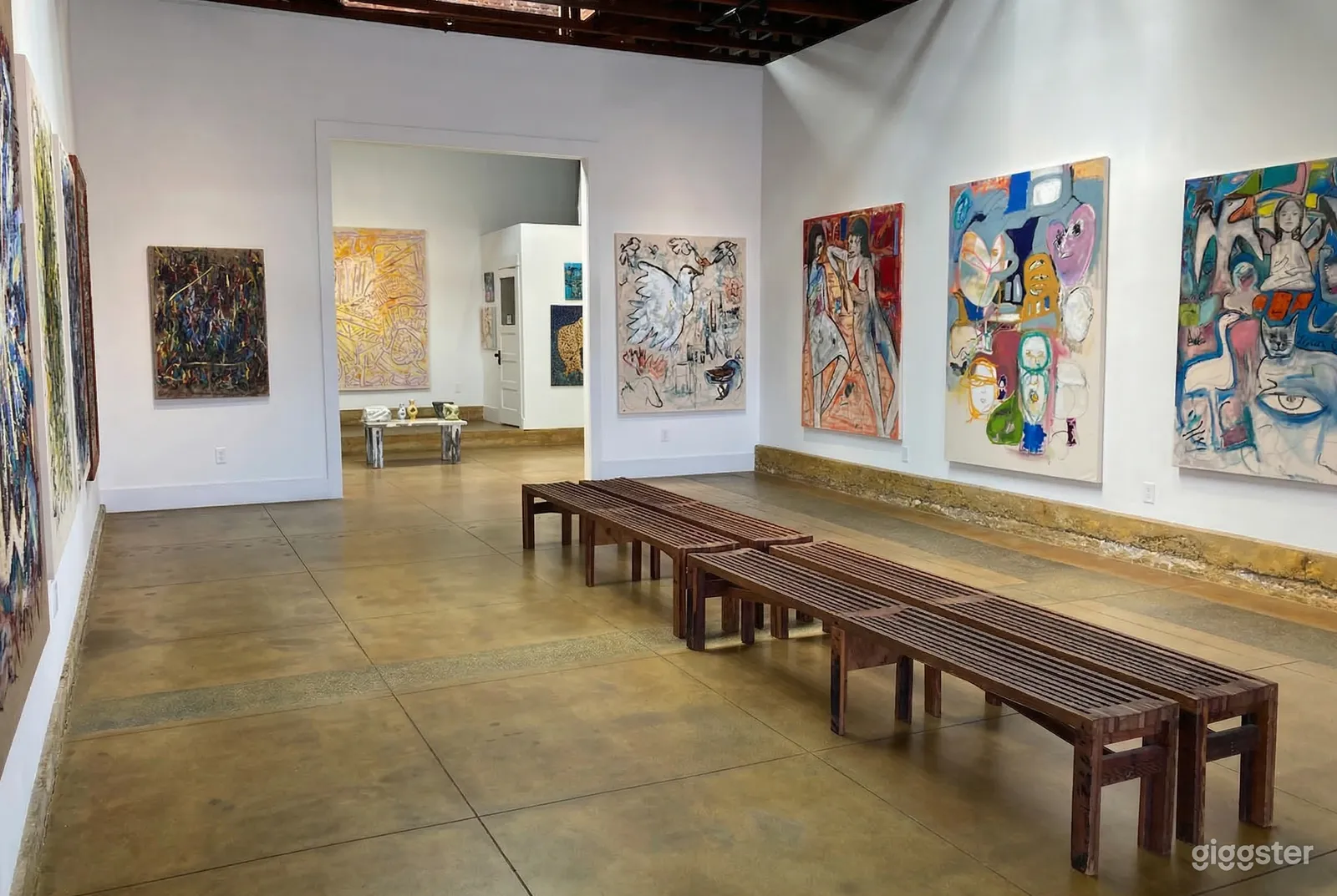 Long wooden benches are central in a gallery space with large colorful paintings on the walls.